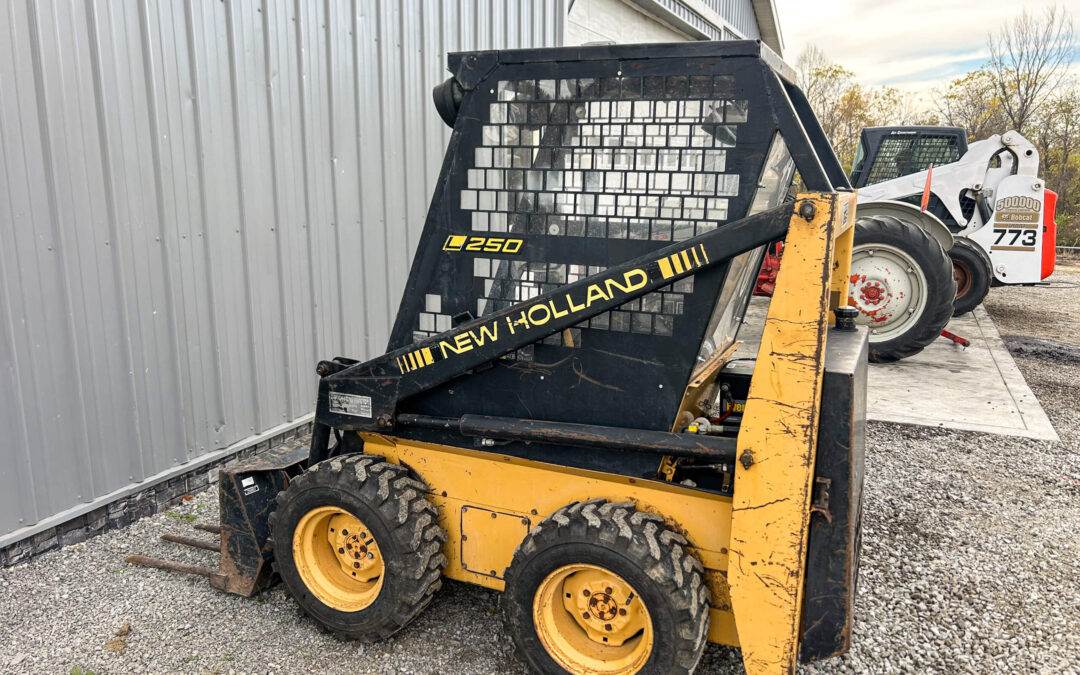 Troyer's Skidloader Repair Rushsylvania, OH A yellow New Holland L250 skid steer loader is parked on gravel beside a metal building, with another loader visible in the background.