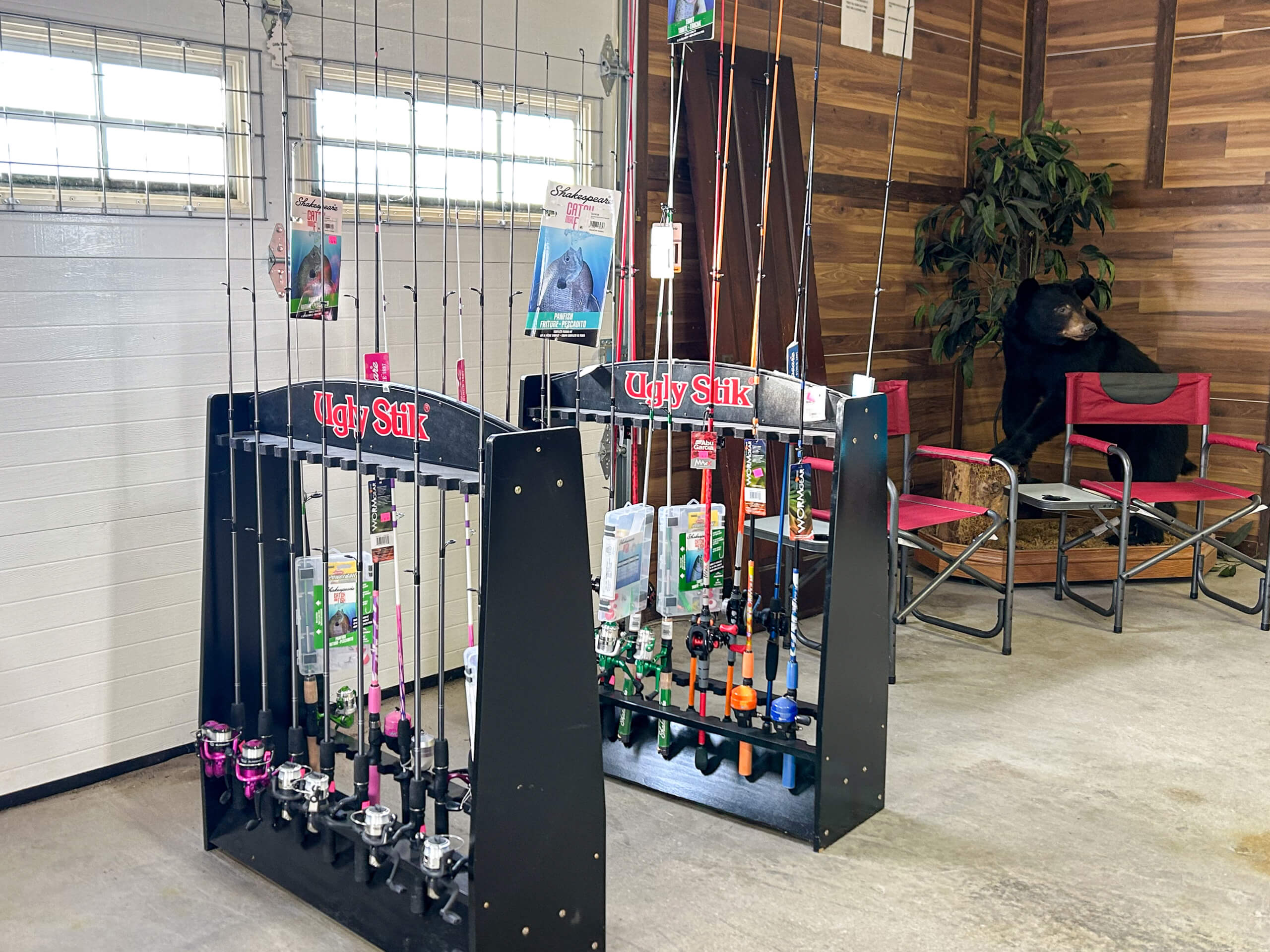 Graber Farm & Home Center Odon Indiana Two racks of fishing rods displayed indoors near a wall with wood paneling; a black bear statue sits beside a red folding chair in the corner.