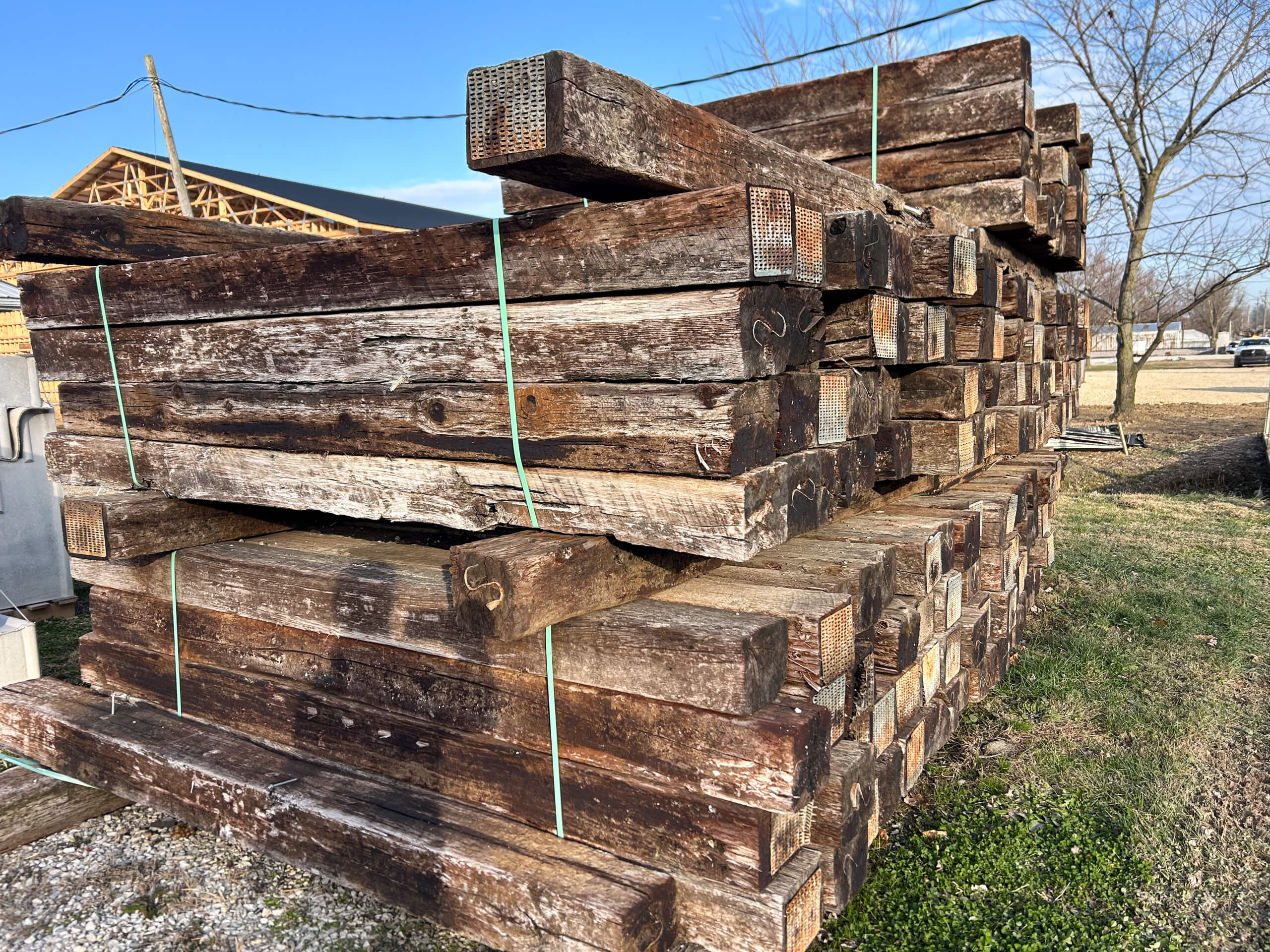 Graber Farm & Home Center Odon Indiana A stack of weathered wooden railroad ties bound with green straps sits outdoors on grass, with a construction site and trees in the background.