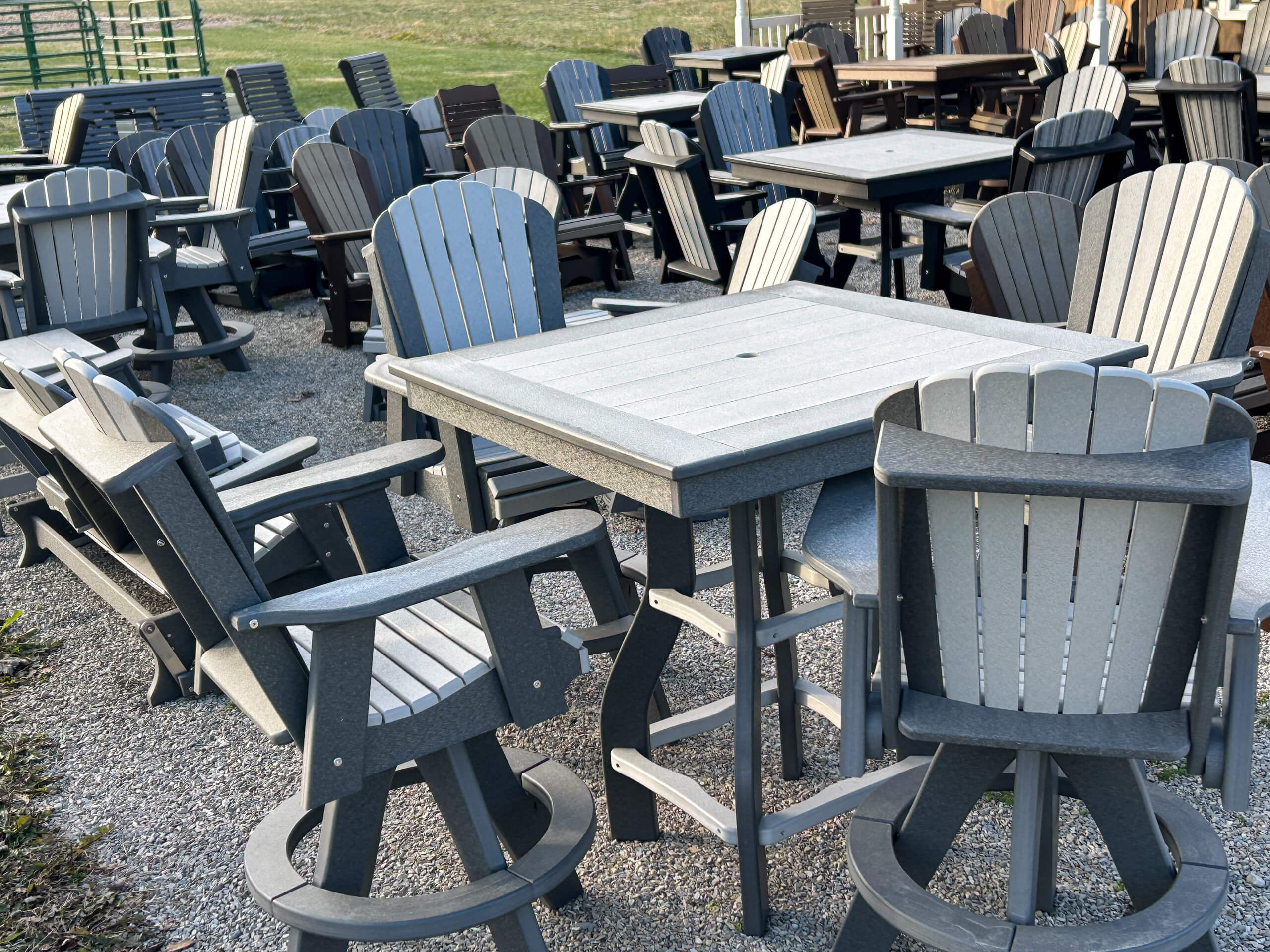 Graber Farm & Home Center Odon Indiana Outdoor patio tables and Adirondack chairs in various shades of gray are arranged in rows on gravel, likely at a furniture store or display area.