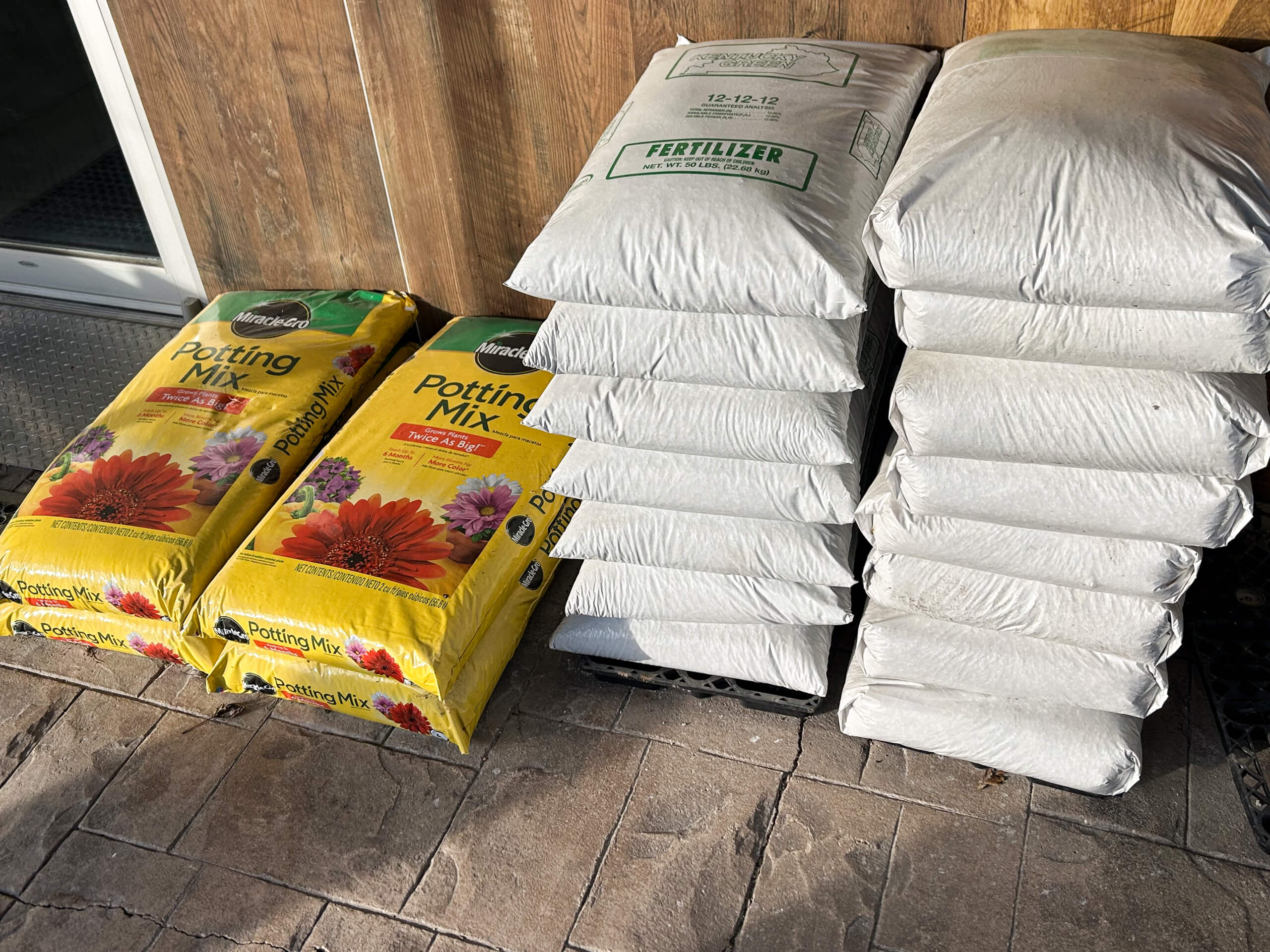Graber Farm & Home Center Odon Indiana Bags of potting mix and fertilizer are stacked on a paved surface next to a building.