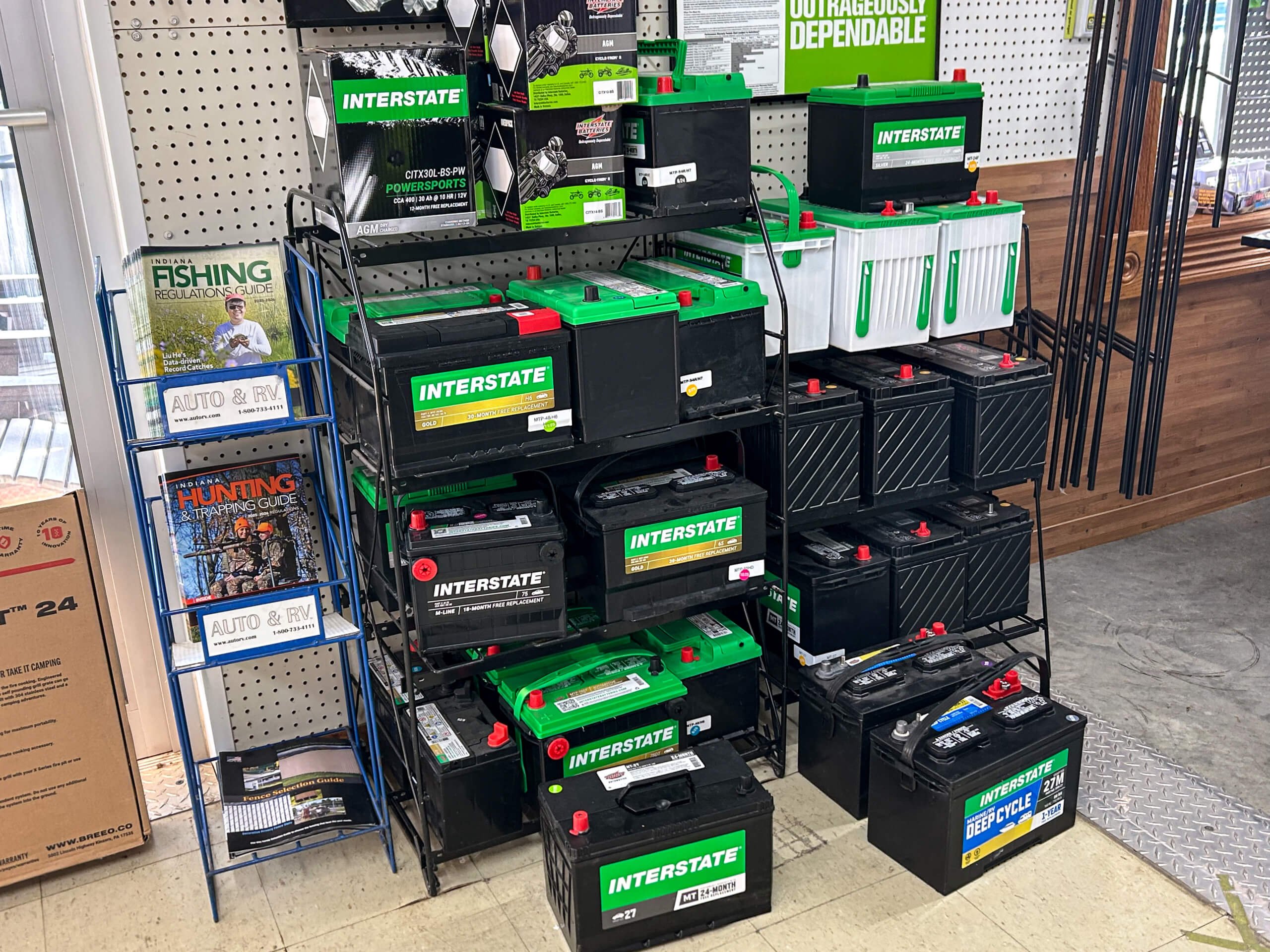 Graber Farm & Home Center Odon Indiana A display of various Interstate car batteries arranged on shelves, next to a magazine rack holding fishing and hunting publications.