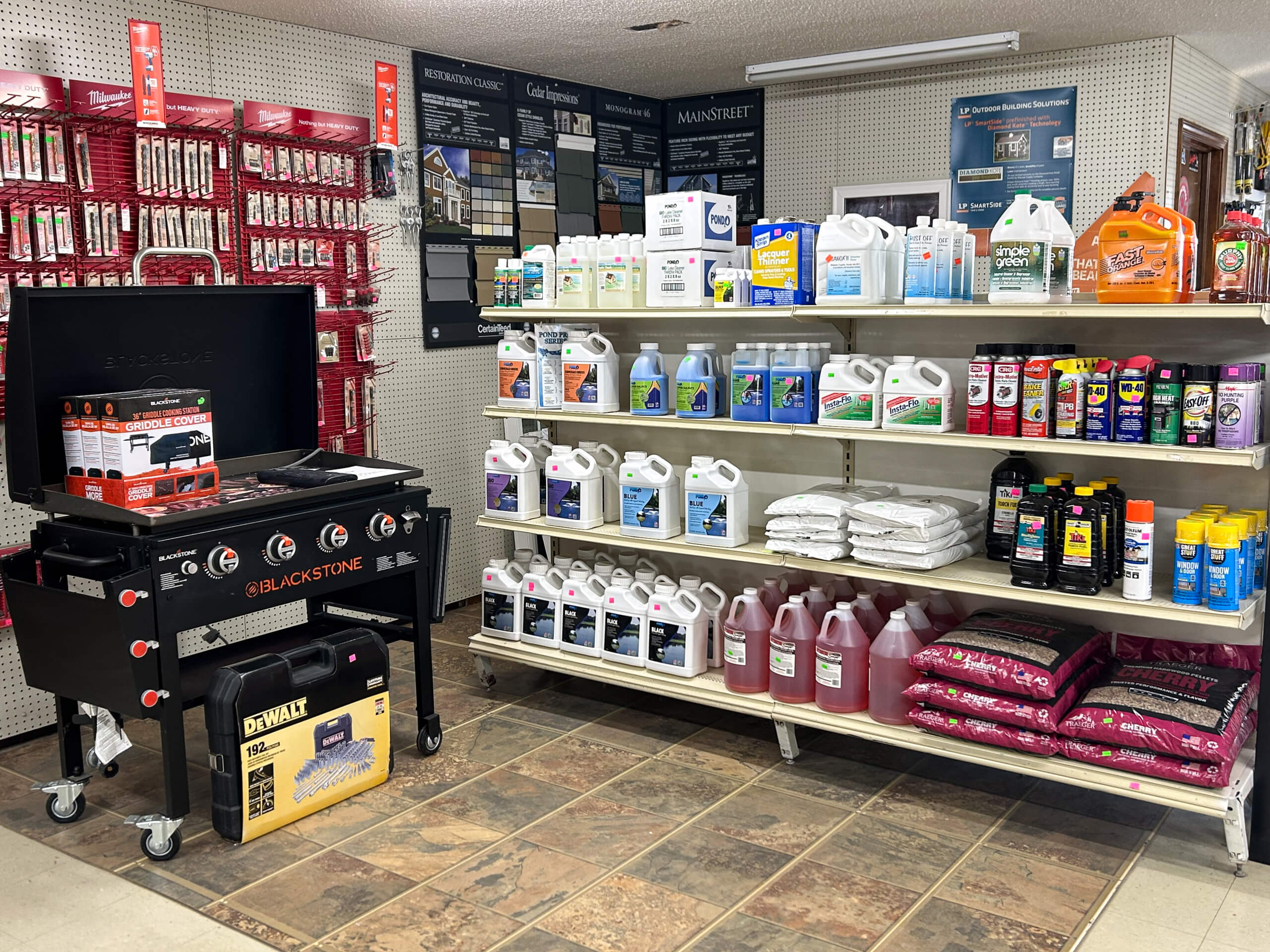 Graber Farm & Home Center Odon Indiana Shelves display cleaning products, fuel cans, automotive fluids, and lawn care supplies; a Blackstone grill and DeWalt toolbox are on the floor, with hardware items hanging on the wall.