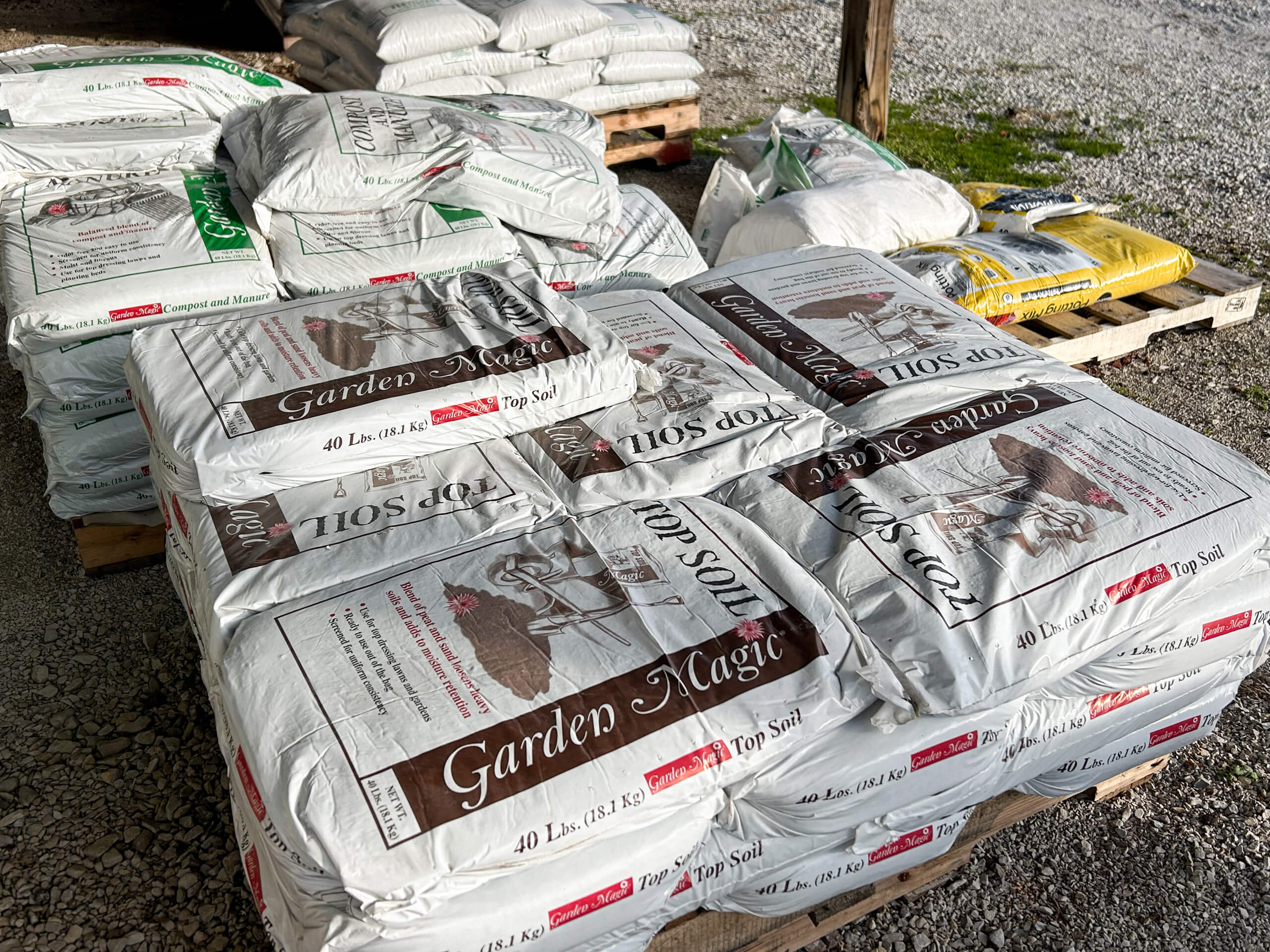 Graber Farm & Home Center Odon Indiana Pallets stacked with 40 lb bags of Garden Magic top soil and other bagged garden supplies on a gravel surface.