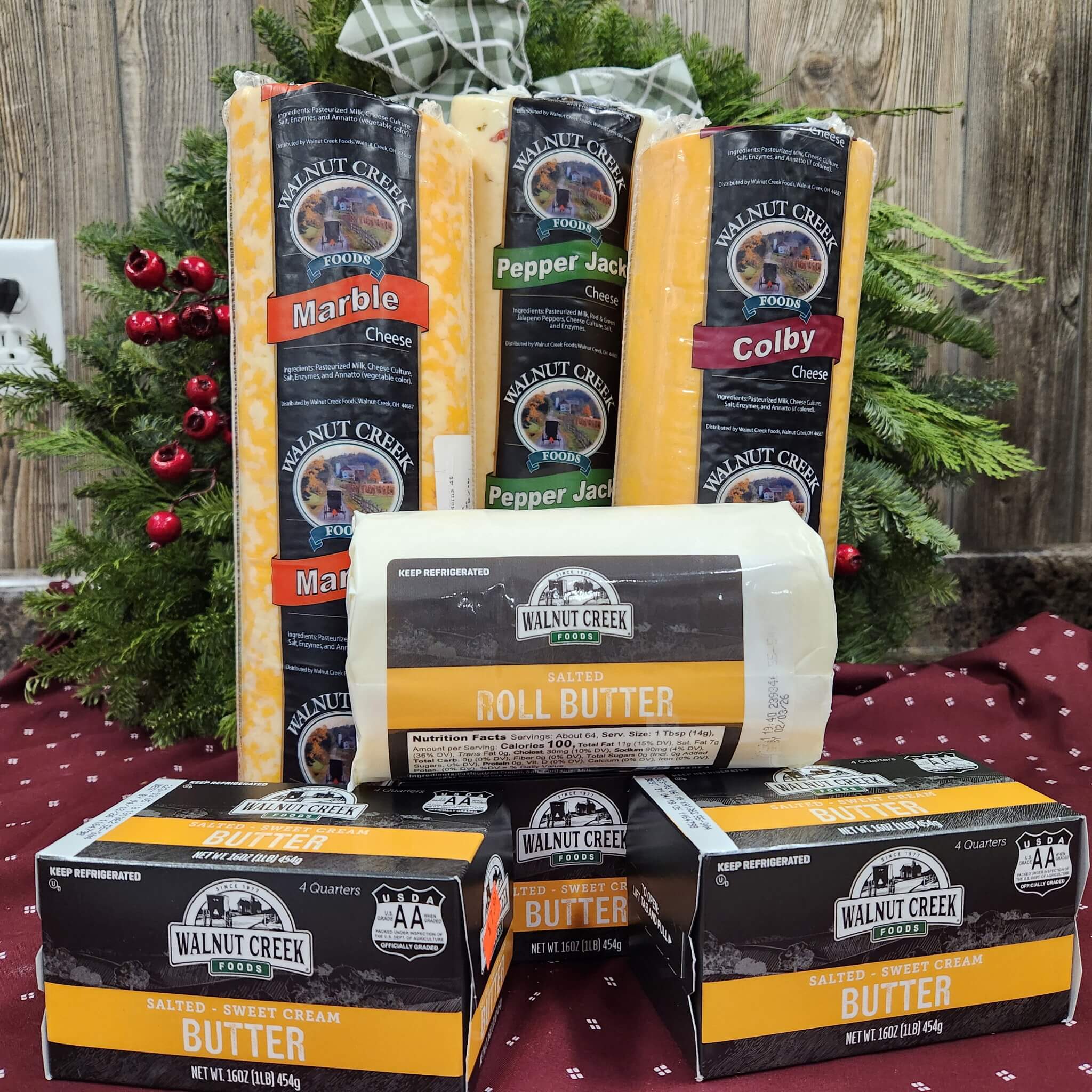 Countrty Pantry Sheridan, MI Several Walnut Creek Foods cheese and butter products are arranged on a table with a festive greenery decoration in the background.