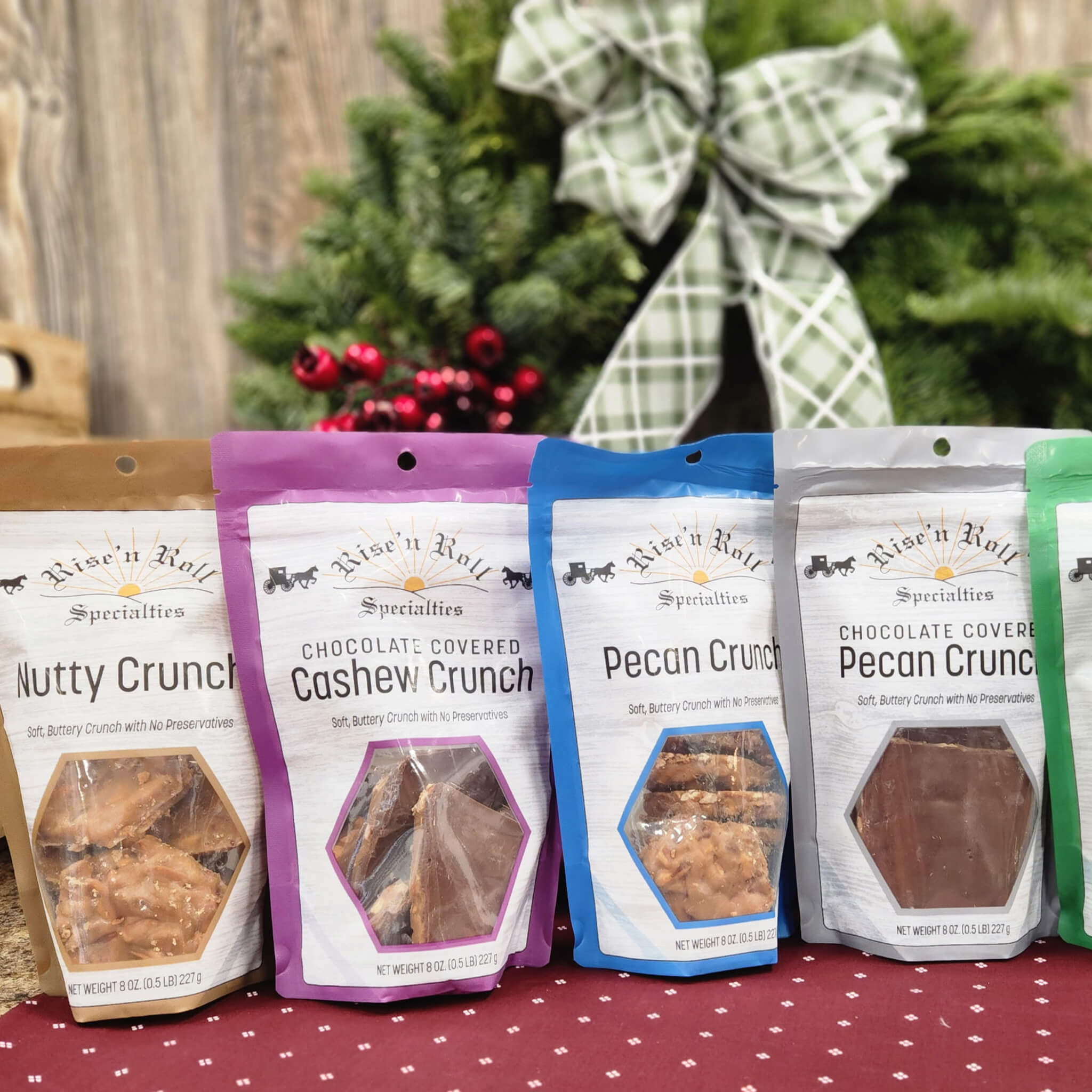 Countrty Pantry Sheridan, MI Five bags of Riseโn Roll Specialties nut and chocolate snacks are displayed on a red polka-dot tablecloth, with a green holiday wreath in the background.