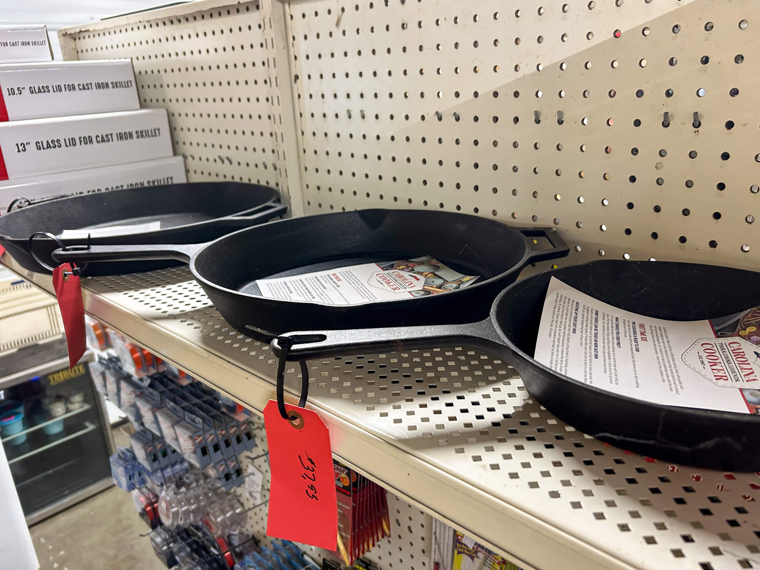 Country Side Harness Centerville MI Three cast iron skillets with red price tags are displayed on a metal store shelf, each containing a product information sheet.