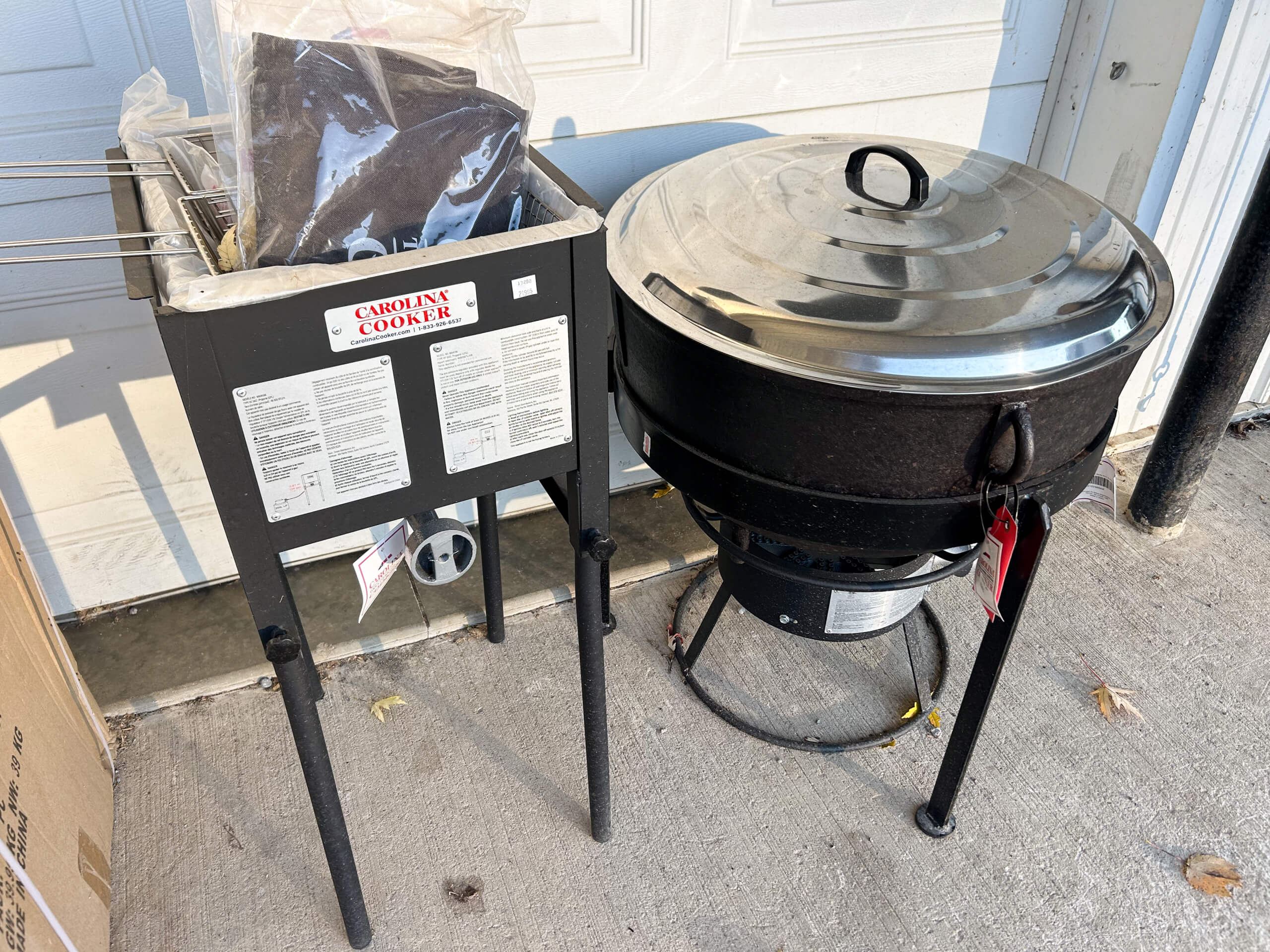 Country Side Harness Centerville MI A metal Carolina Cooker with instructions stands next to a large round black covered outdoor cooker on a concrete surface.