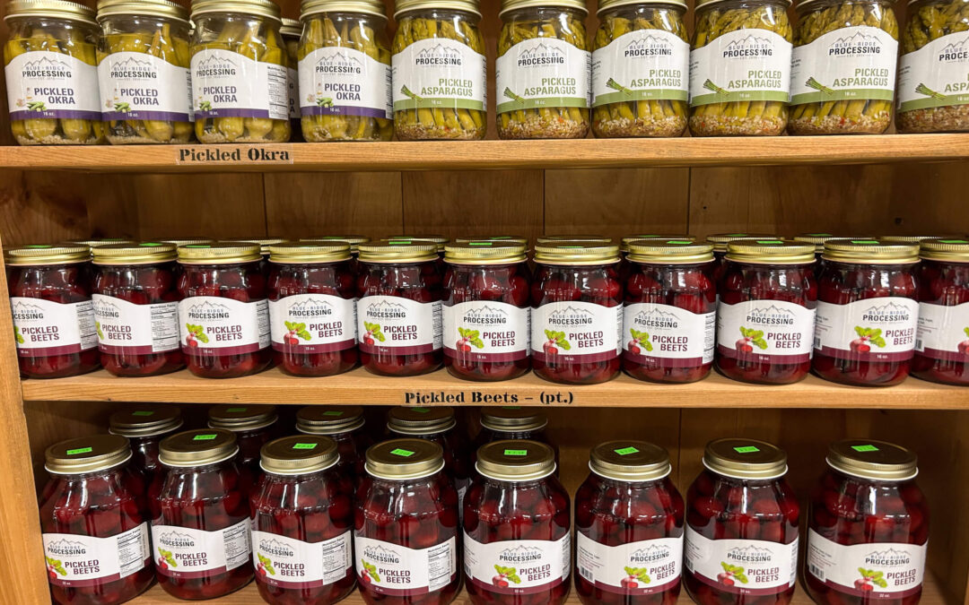 Millcreek Market Junction City Ohio Jars of pickled okra, pickled asparagus, and pickled beets are neatly arranged on wooden shelves at a store.