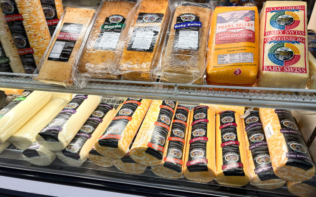 Millcreek Market Junction City Ohio A refrigerated display case filled with assorted packaged cheeses, including gouda, Swiss, Colby Jack, mozzarella, and pepper jack.