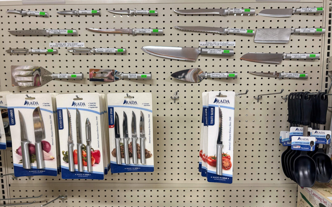 Millcreek Market Junction City Ohio A display of various kitchen knives and utensils, including packaged knife sets and loose knives, arranged on a pegboard wall in a store.