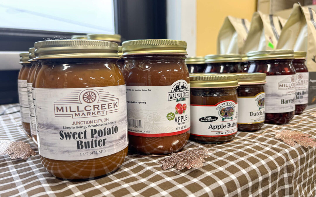 Millcreek Market Junction City Ohio Jars of assorted fruit spreads, including sweet potato butter and apple butter, are displayed on a checkered tablecloth.