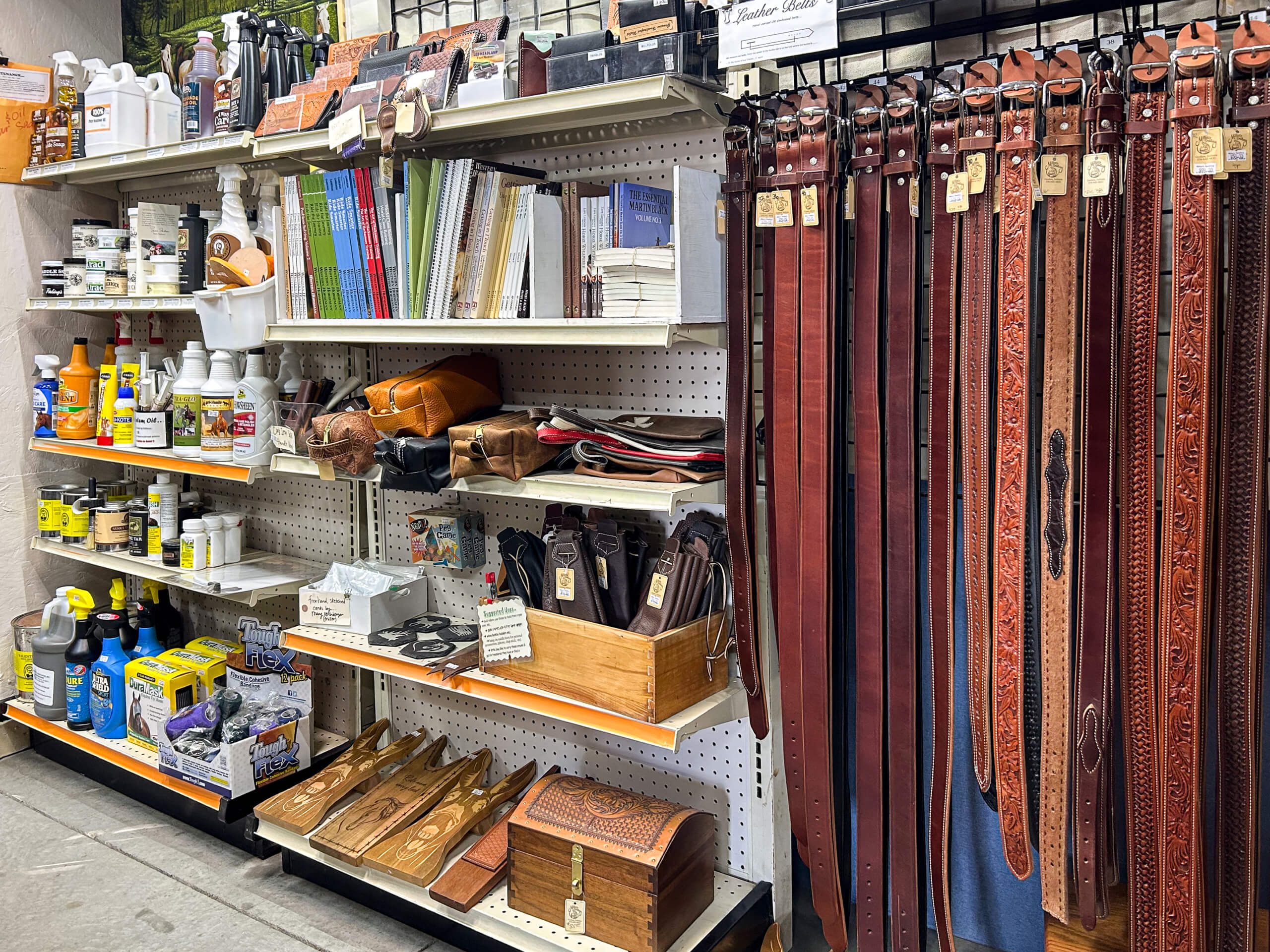 Miller's Saddlery Goshen IN Store shelves display leather belts, bottles of cleaner, books, small leather goods, wooden boxes, and various horse tack supplies organized neatly.