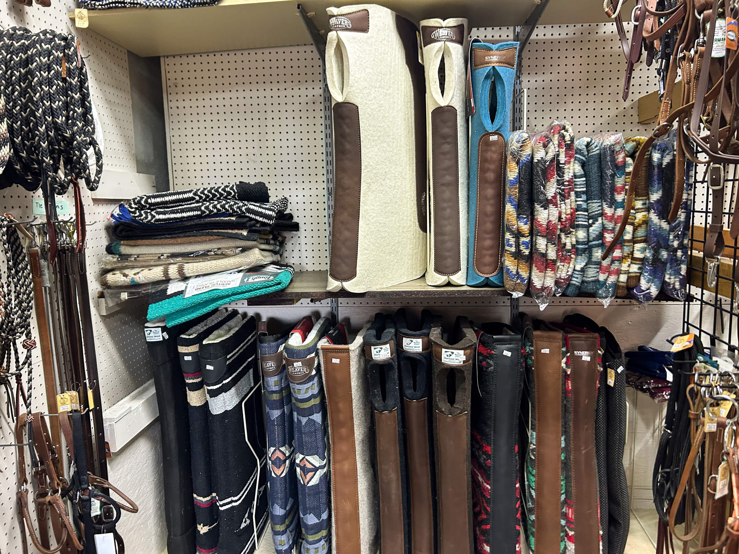 Miller's Saddlery Goshen IN Shelves display saddle pads, stirrup covers, and horse riding gear in various colors and patterns at a tack store.