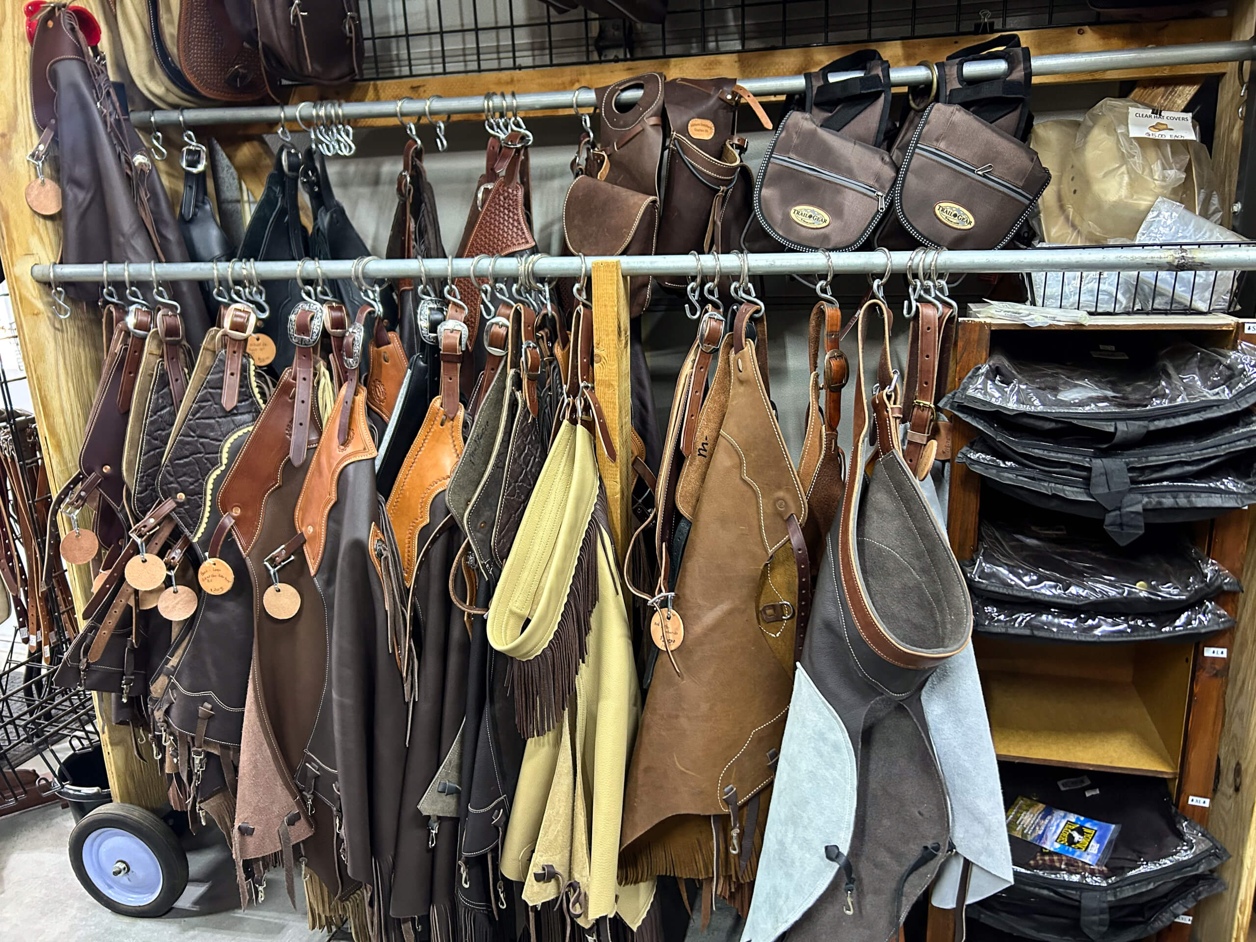 Miller's Saddlery Goshen IN Various leather chaps and accessories hang on racks in a store, with shelves of folded items and bags visible to the right.