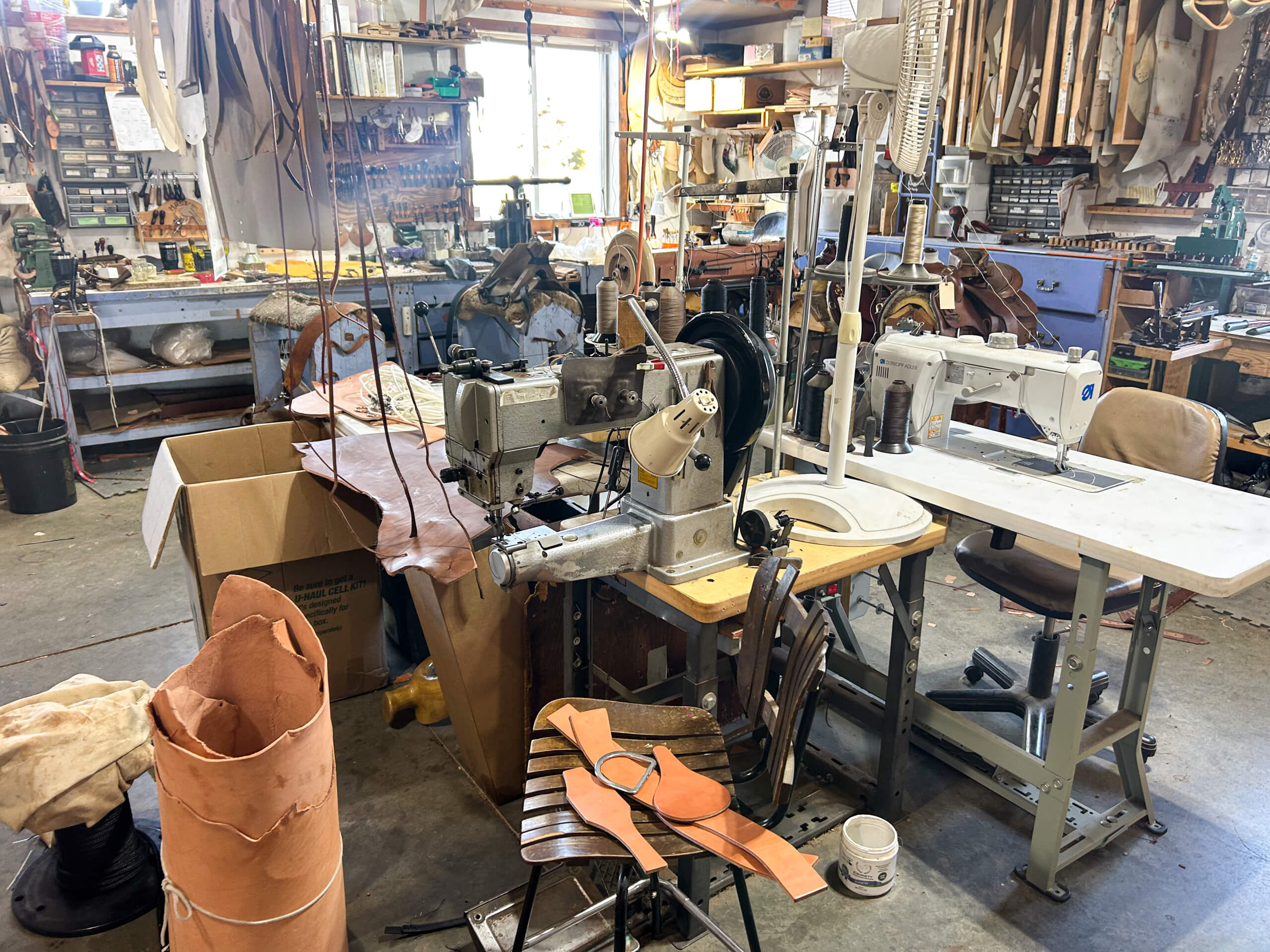 Miller's Saddlery Goshen IN A leather workshop with sewing machines, leather pieces, tools, rolls of leather, and various supplies organized around the workspace.