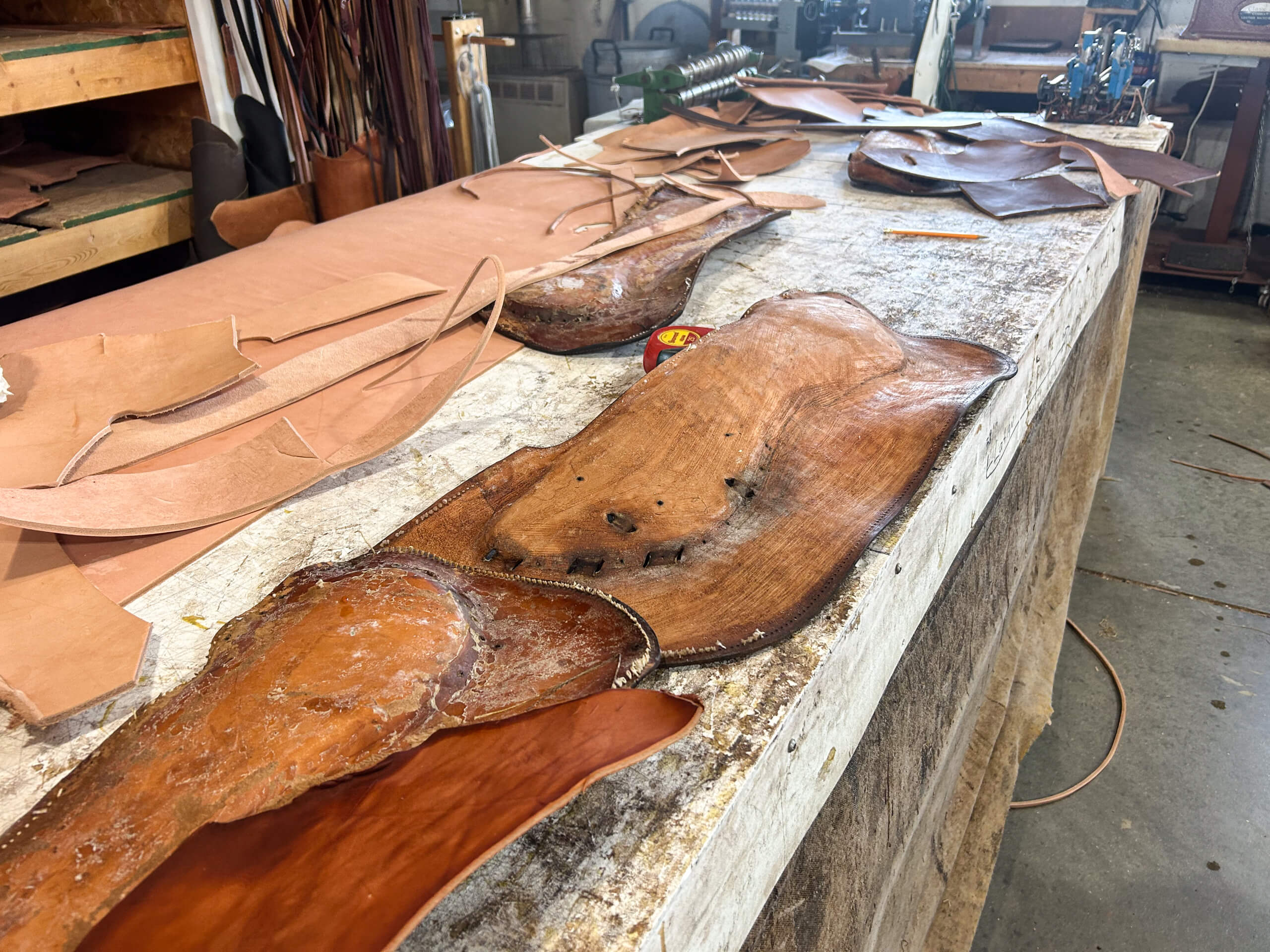 Miller's Saddlery Goshen IN A workbench covered with various pieces of cut and raw leather in a workshop setting, with tools and shelves visible in the background.