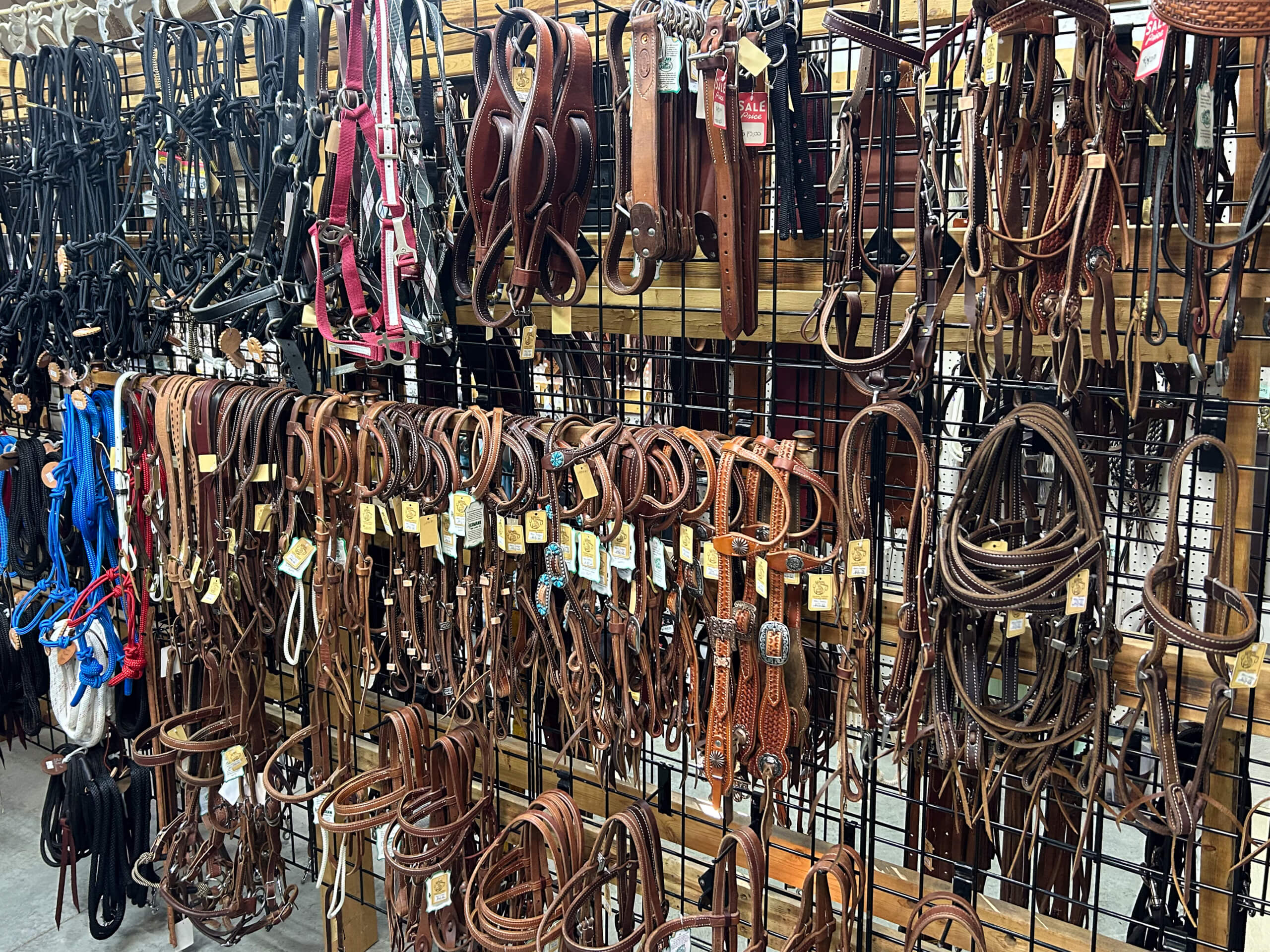 Miller's Saddlery Goshen IN Various horse bridles and reins in different colors and styles are hanging on a metal grid wall display in a tack shop.