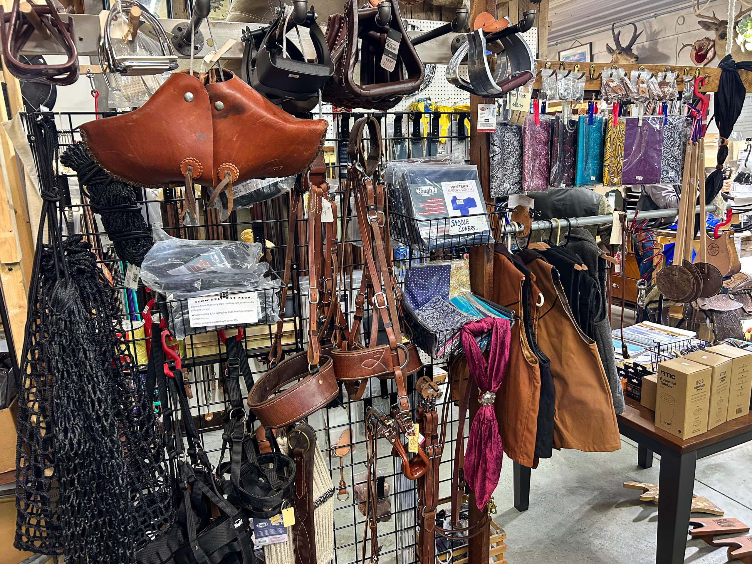 Miller's Saddlery Goshen IN Display of leather harnesses, ropes, bags, scarves, and various accessories organized on racks in a store setting.