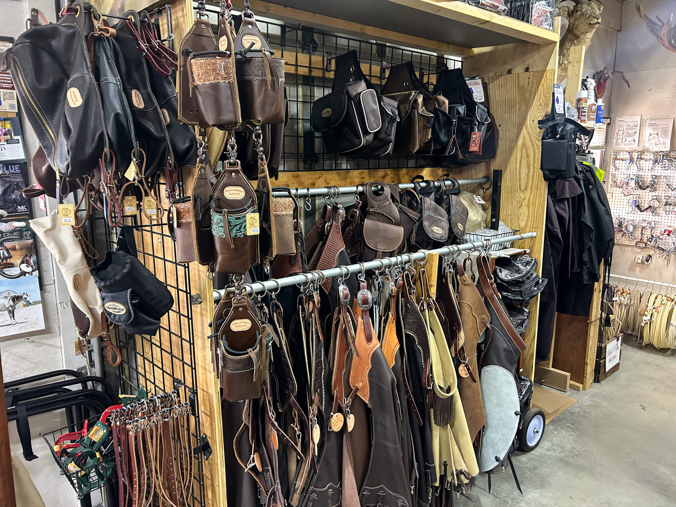 Miller's Saddlery Goshen IN Display of leather bags, pouches, and accessories hanging on racks and hooks in a store with various merchandise visible in the background.