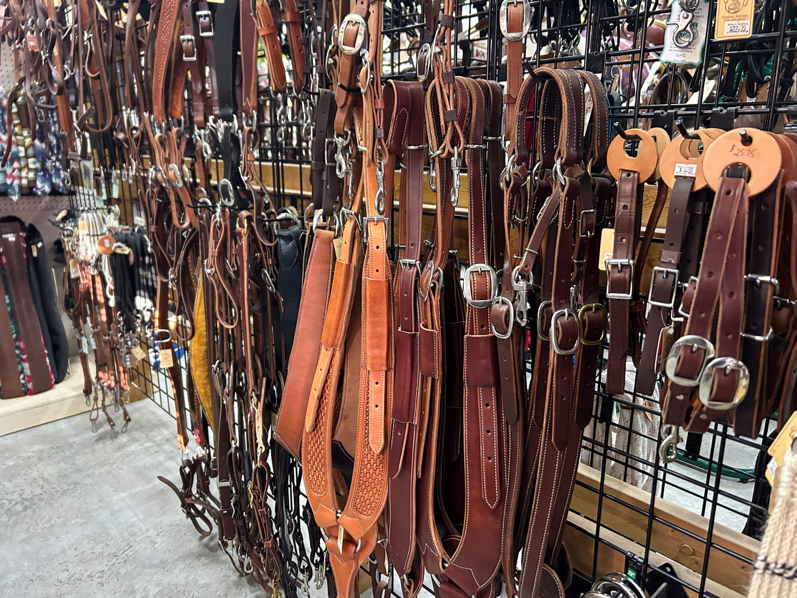 Miller's Saddlery Goshen IN Assorted leather horse tack, including bridles and reins, hanging on a metal grid display in a store.