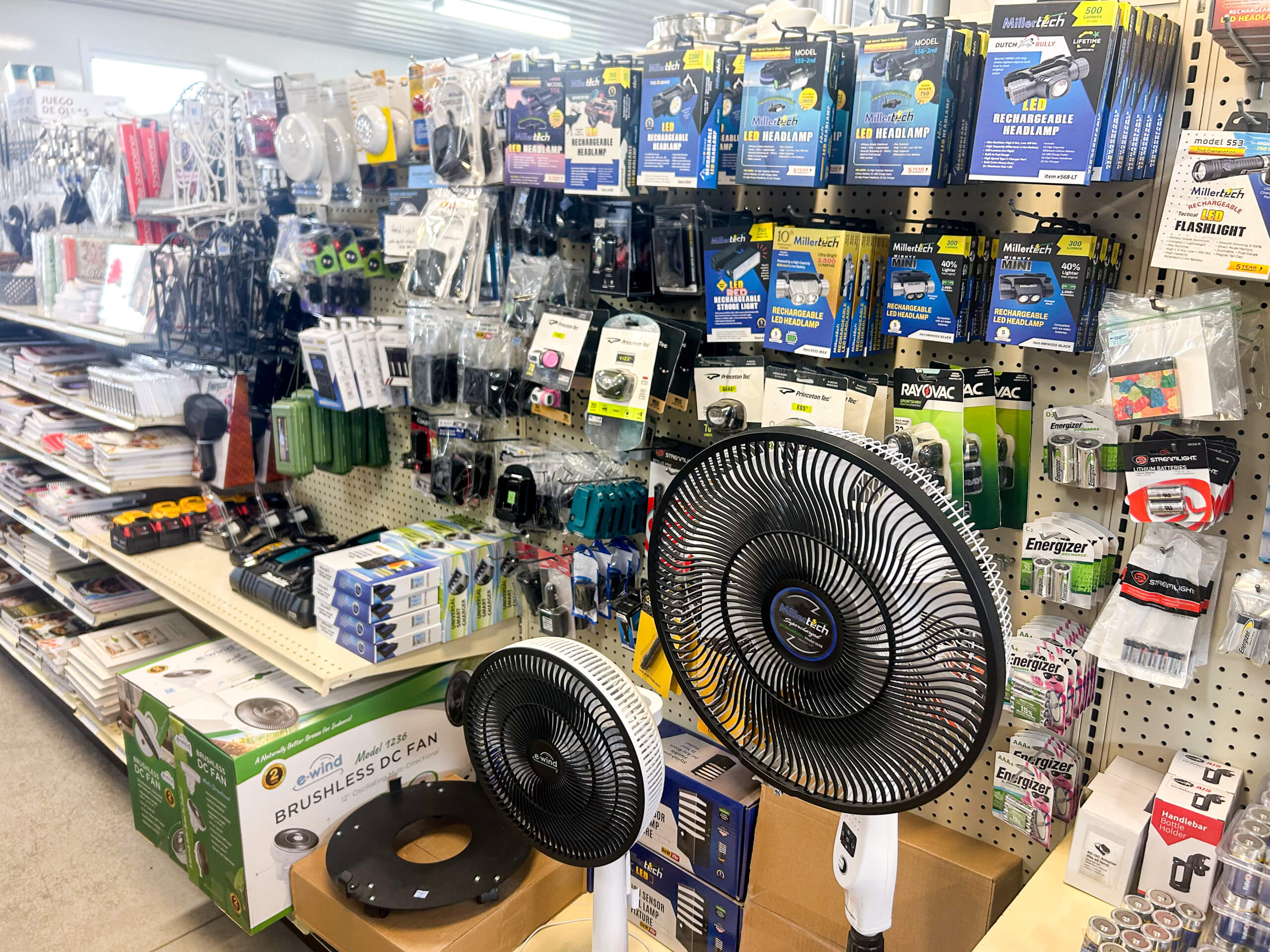 Miller's Variety Store Etna Green, IN Shelves of hardware and electrical supplies, including fans, batteries, extension cords, and small tools, displayed in a well-lit store aisle.