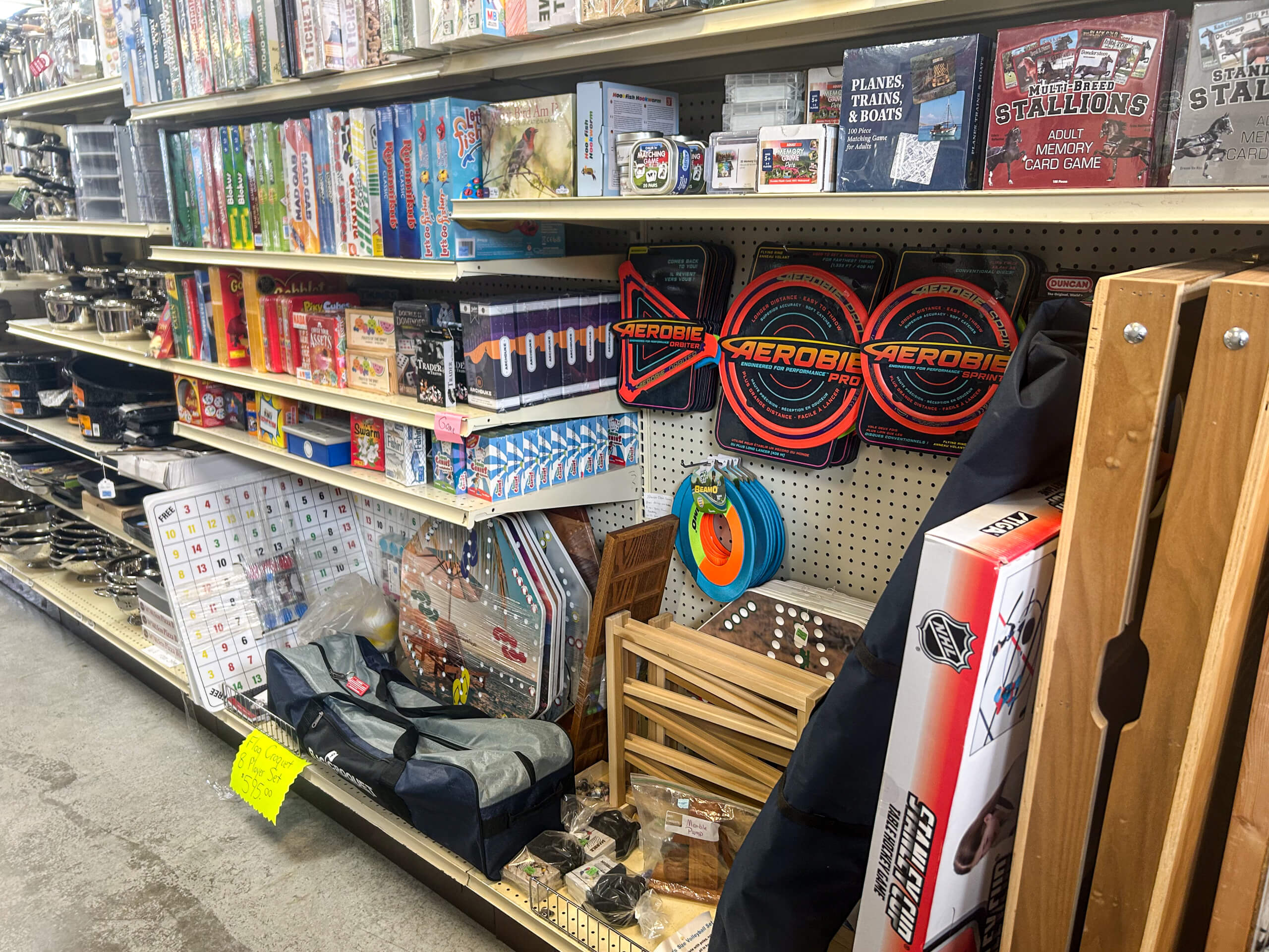 Miller's Variety Store Etna Green, IN Shelves stocked with board games, puzzles, Aerobie flying discs, wooden game sets, and various recreational items in a store aisle.