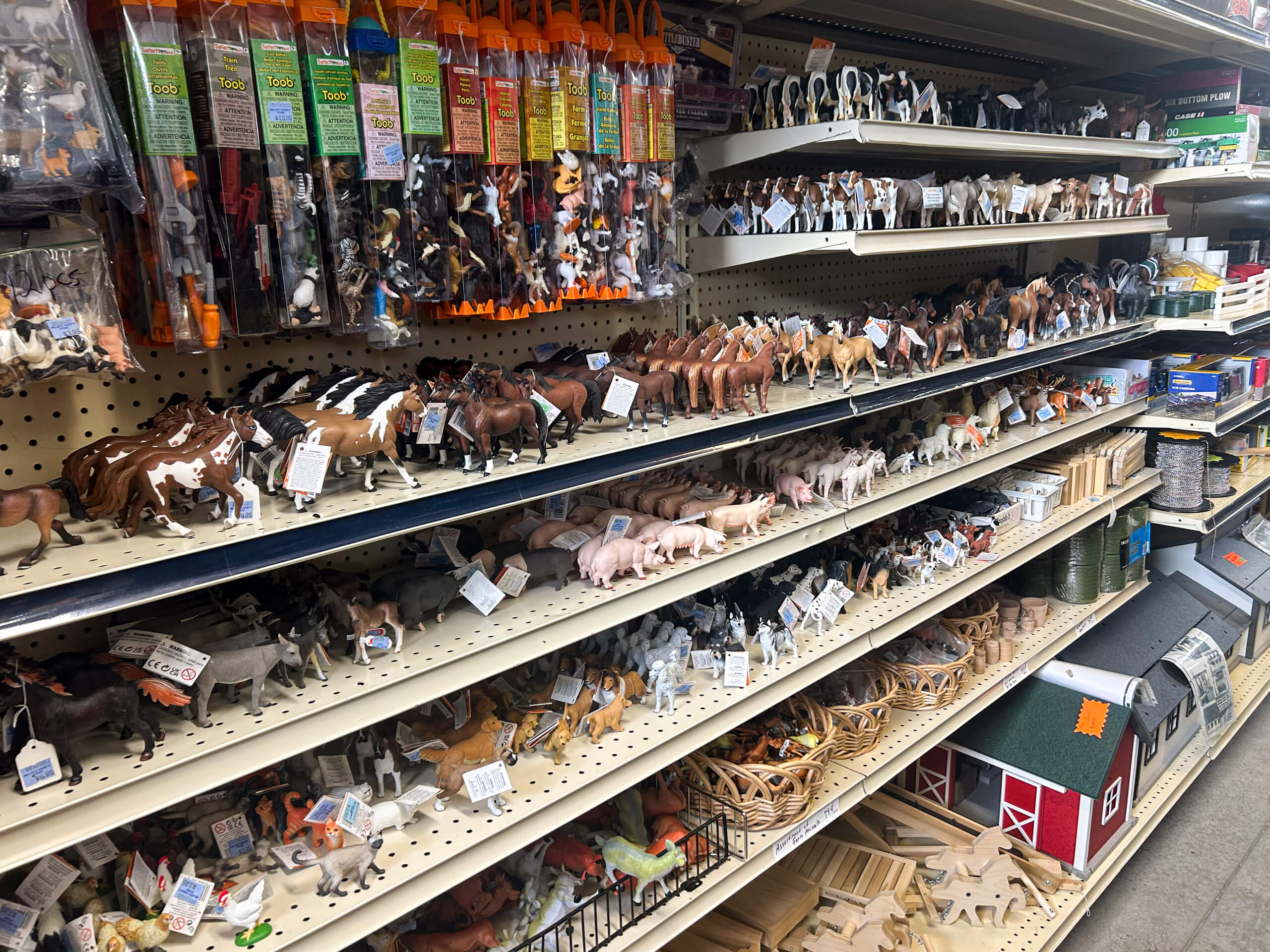 Miller's Variety Store Etna Green, IN Shelves stocked with various plastic animal figurines, including cows, horses, pigs, and more, organized by type in a store aisle.