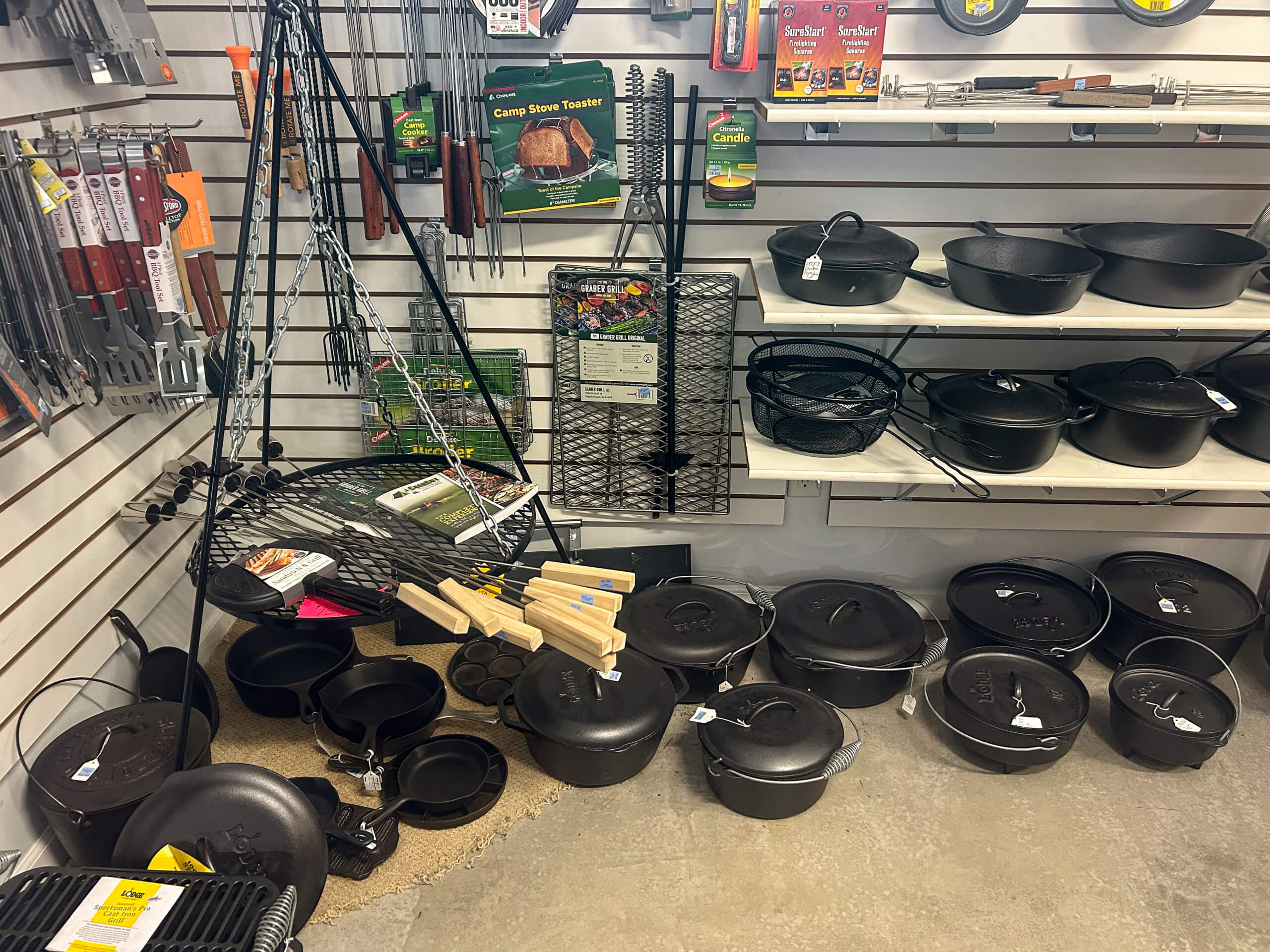 Miller's Variety Store Etna Green, IN Display of cast iron cookware, including Dutch ovens, pans, and grilling accessories, arranged on shelves and the floor in a store.