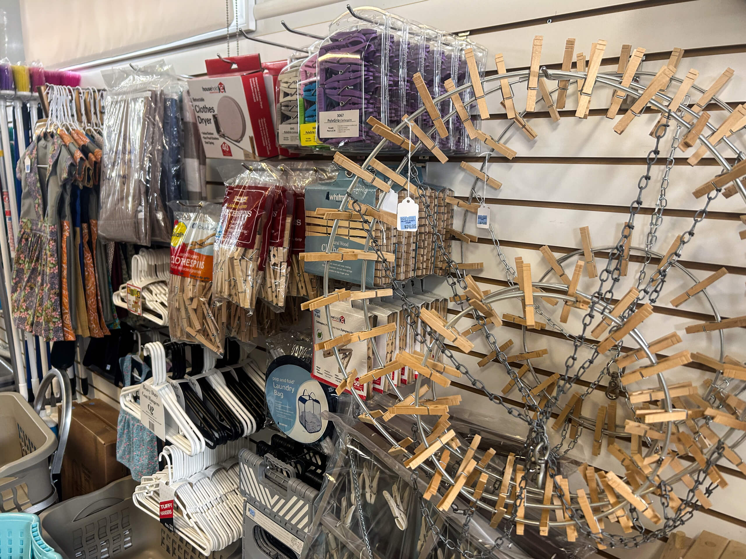 Miller's Variety Store Etna Green, IN Various laundry and household items, including clothespins, hangers, drying racks, and fabric items, displayed on a store wall and shelves.