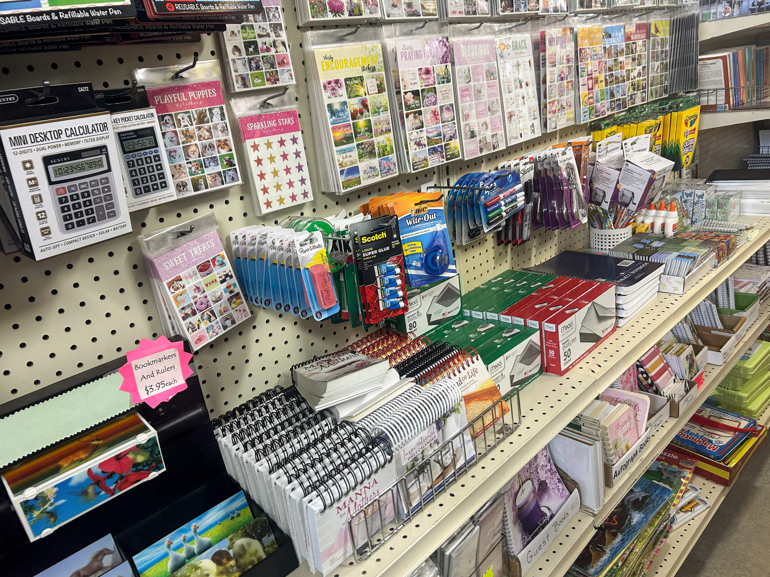 Miller's Variety Store Etna Green, IN A store shelf stocked with calculators, pens, notepads, tape, packs of stickers, and various stationery supplies.