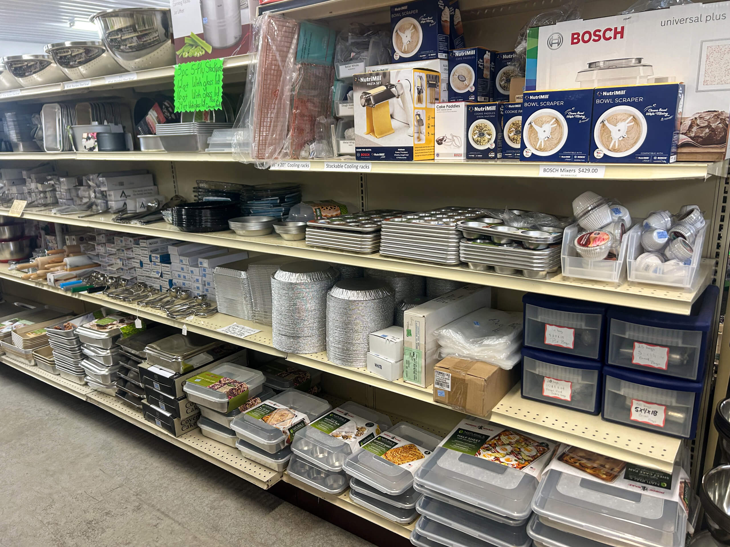 Miller's Variety Store Etna Green, IN Store aisle shelf stocked with various kitchenware items including trays, containers, cake pans, baking dishes, mixing bowls, and boxed appliances.
