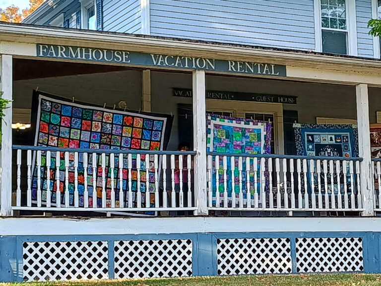 Weaver-View Farms Quilting Retreats Penn Yan, NY A farmhouse vacation rental with colorful quilts hanging on the front porch railing.