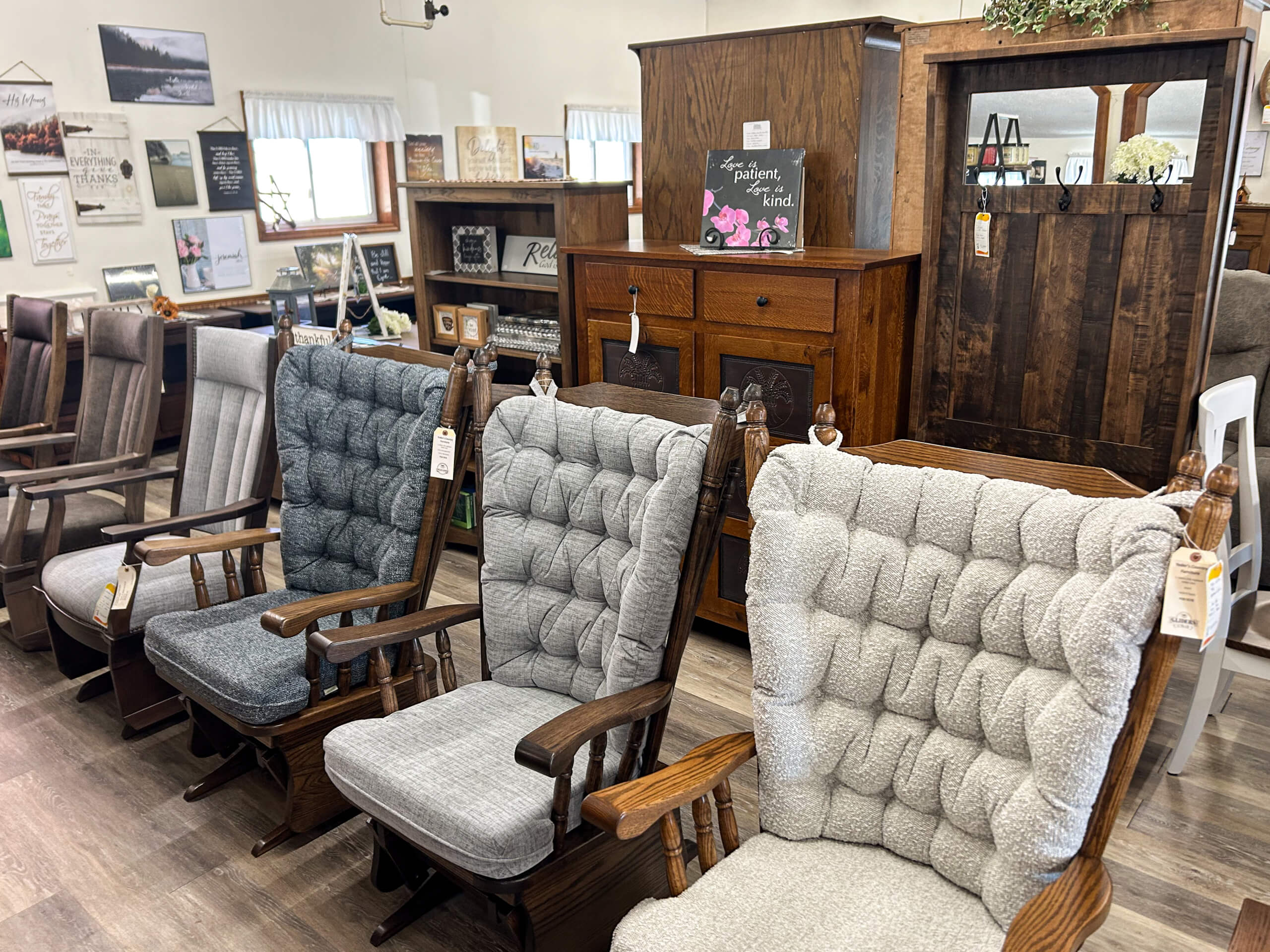 Yolder's Country Furniture Belle Center OH A display of cushioned wooden rocking chairs in a furniture store, with various wooden cabinets and wall art in the background.