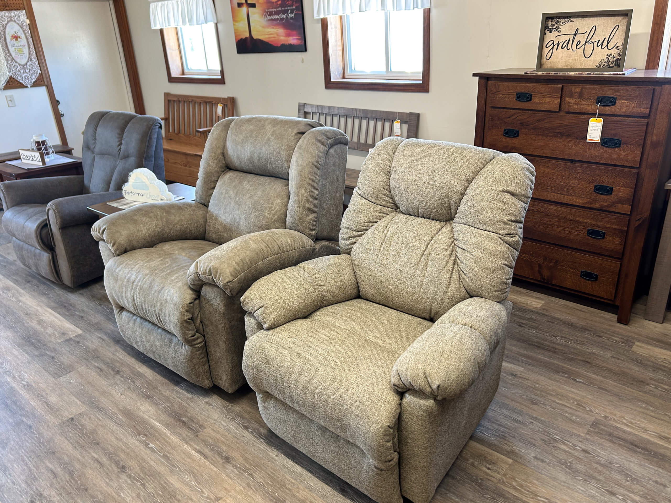Yolder's Country Furniture Belle Center OH Two gray upholstered recliner chairs are displayed in a furniture showroom with wood flooring and additional wooden furniture in the background.