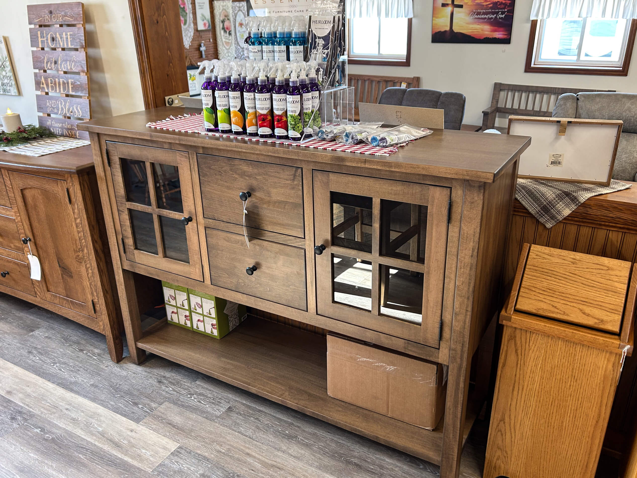 Yolder's Country Furniture Belle Center OH Wooden sideboard with two glass-front cabinets, two central drawers, and display items on top, situated in a store with other furniture pieces nearby.
