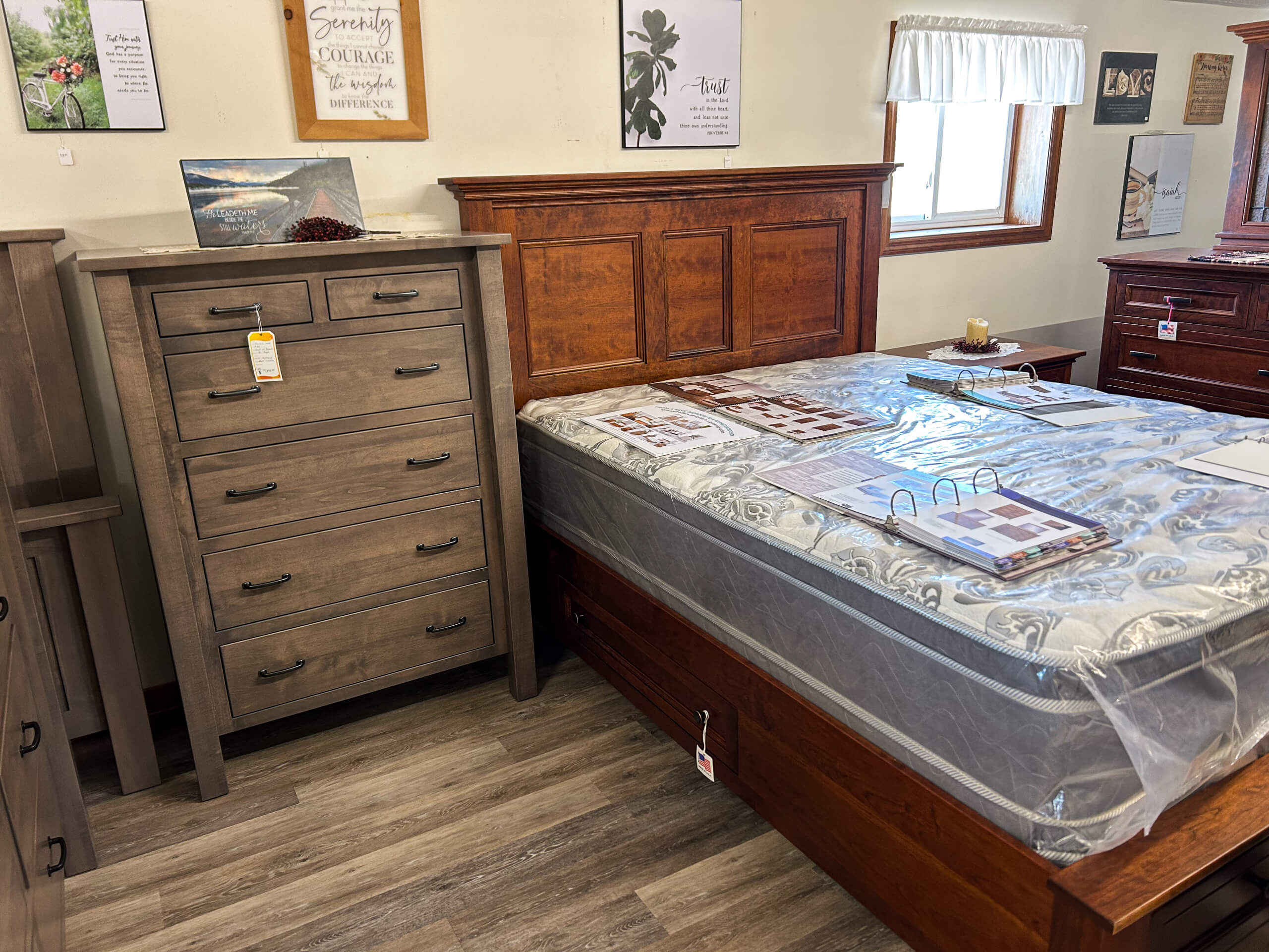 Yolder's Country Furniture Belle Center OH A wooden dresser and bed with a mattress in a showroom, surrounded by decor and informational materials.