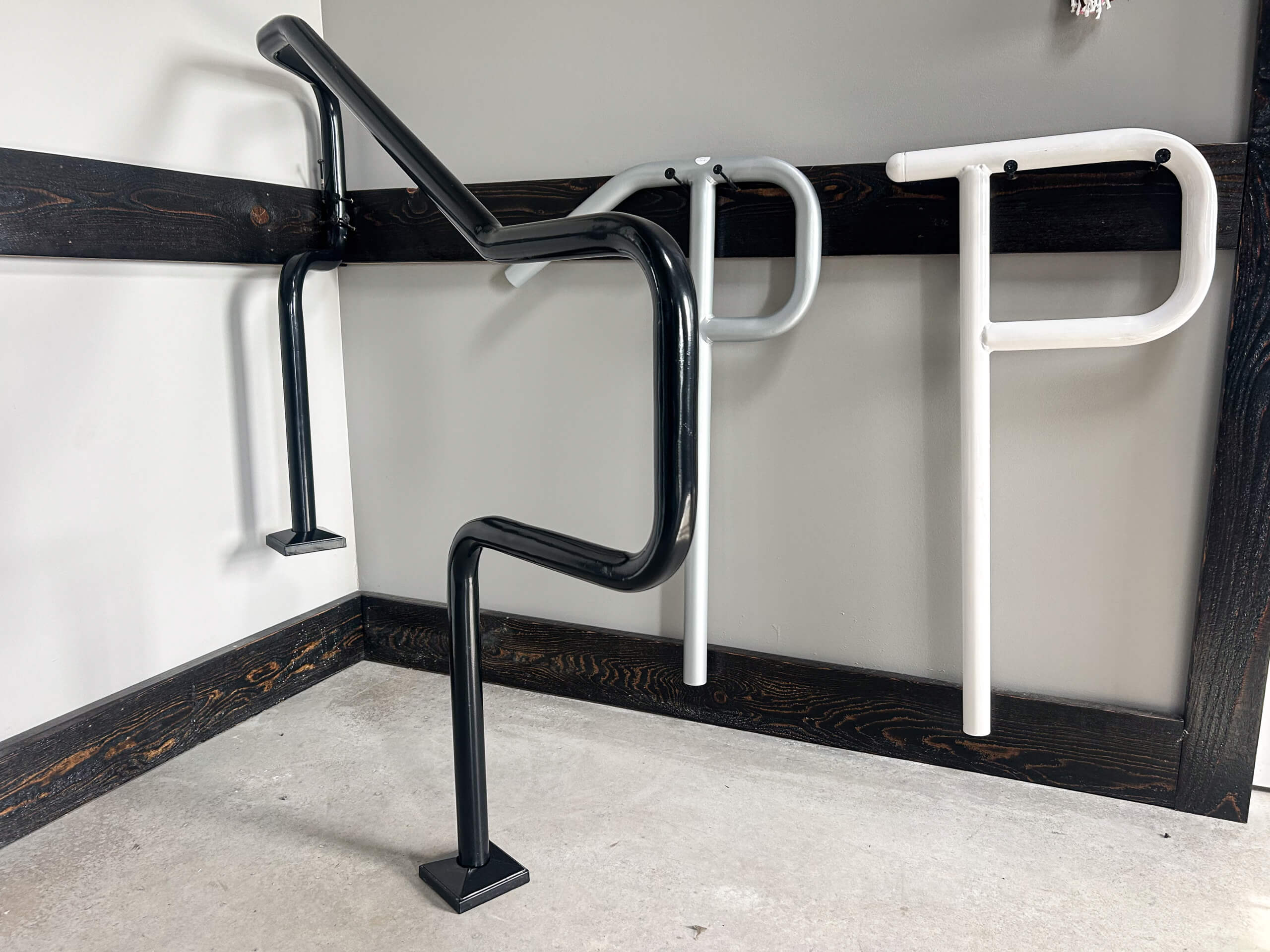 Zook's Metal Fabricating & Railings Allenwood, PA Three metal handrails shaped like the letters R, P, and P, mounted on the walls of a corner, with two white and one black handrail.