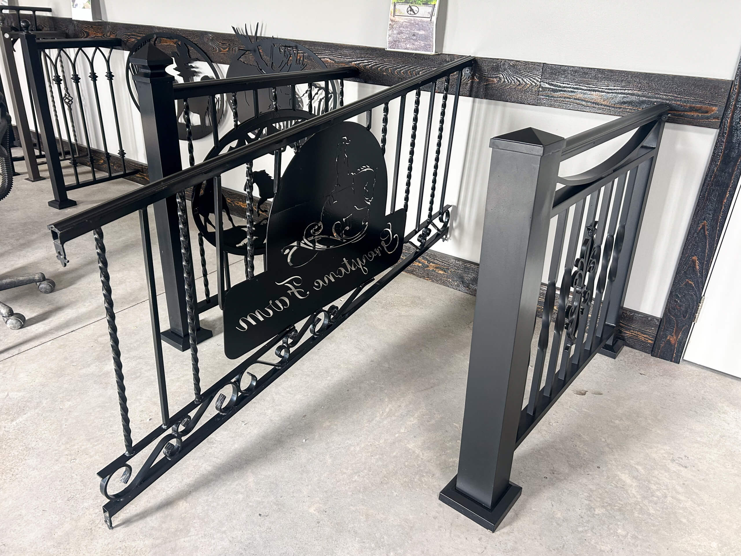 Zook's Metal Fabricating & Railings Allenwood, PA A black metal handrail and gate with decorative scrollwork and an engraved sign reading "Stephanie’s Farm," displayed indoors on a concrete floor.