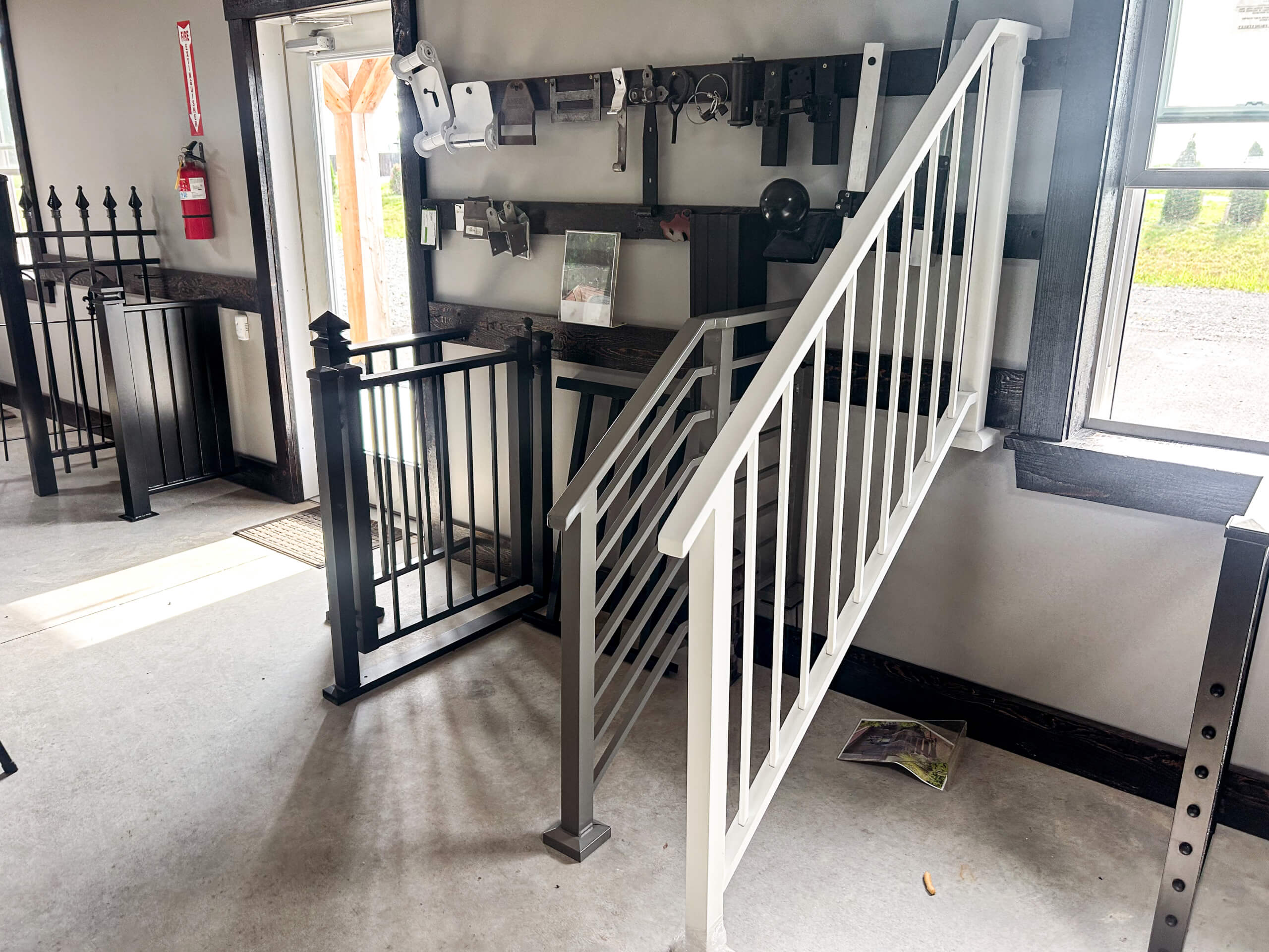 Zook's Metal Fabricating & Railings Allenwood, PA A display of railing and gate samples in a showroom, including a small staircase with white railings and a black metal gate.