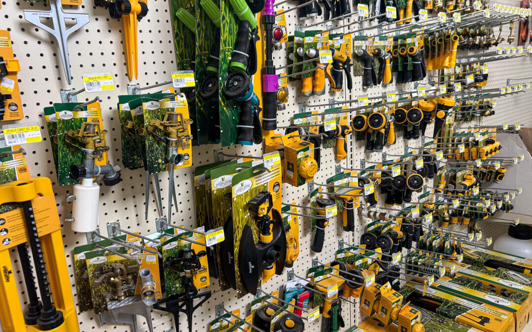 Shetler's Supplies Hardware Variety Bulk Foods Greenville PA Display of various garden hoses, nozzles, sprayers, and accessories in yellow and green packaging arranged on a pegboard wall in a store aisle.