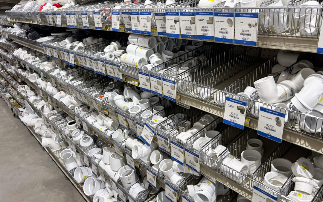 Shetler's Supplies Hardware Variety Bulk Foods Greenville PA Shelves in a hardware store display various types of white PVC pipe fittings organized in metal bins with labels and price tags.