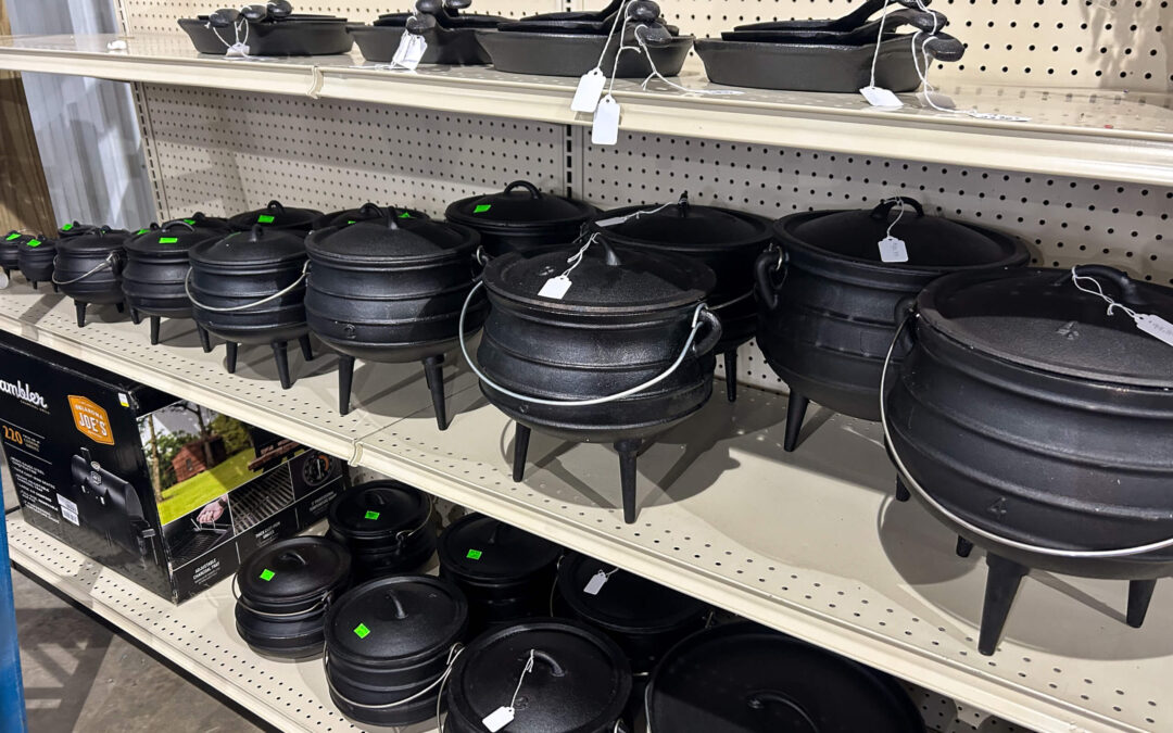 Shetler's Supplies Hardware Variety Bulk Foods Greenville PA Shelves display various sizes of black cast iron pots with lids and handles, alongside cast iron cookware, all with price tags attached.