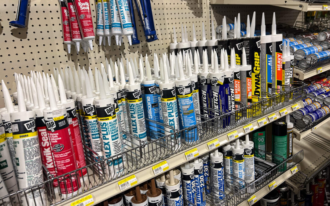 Shetler's Supplies Hardware Variety Bulk Foods Greenville PA Shelves stocked with various types and brands of caulk and sealant tubes in a hardware store aisle.