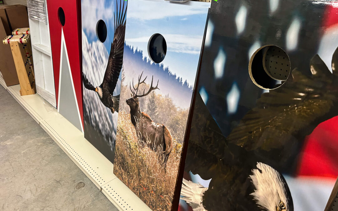 Shetler's Supplies Hardware Variety Bulk Foods Greenville PA Four cornhole boards with various patriotic and wildlife designs displayed upright on a store shelf.