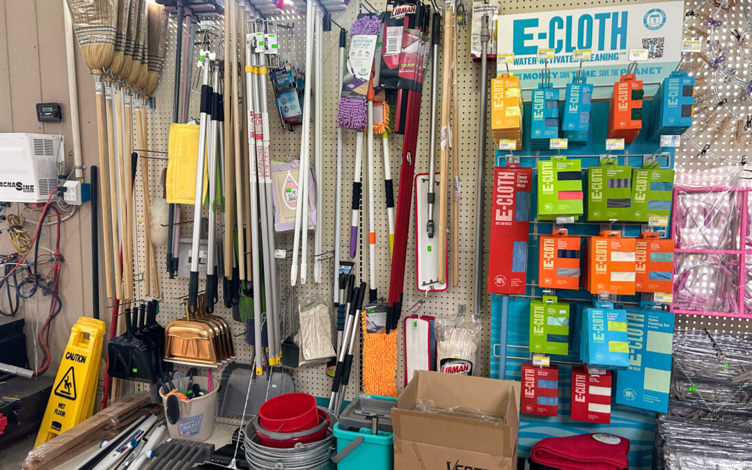 Shetler's Supplies Hardware Variety Bulk Foods Greenville PA Cleaning supplies on display, including brooms, mops, buckets, caution sign, and E-Cloth cleaning cloths, arranged on shelves and pegboards in a store setting.