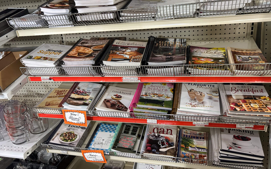 Shetler's Supplies Hardware Variety Bulk Foods Greenville PA Metal shelves display an assortment of cookbooks and kitchenware, including glass measuring cups and recipe journals, in a store aisle.