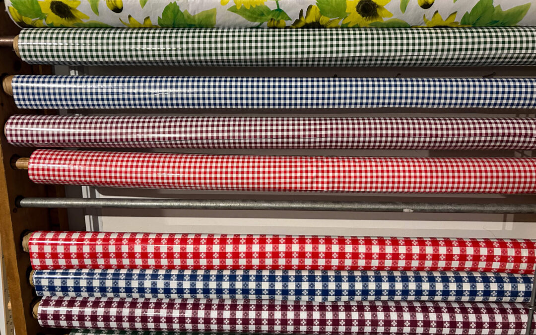 Shetler's Supplies Hardware Variety Bulk Foods Greenville PA Several rolls of patterned fabric, including sunflowers, gingham, and checkered designs, are stacked horizontally on shelves.