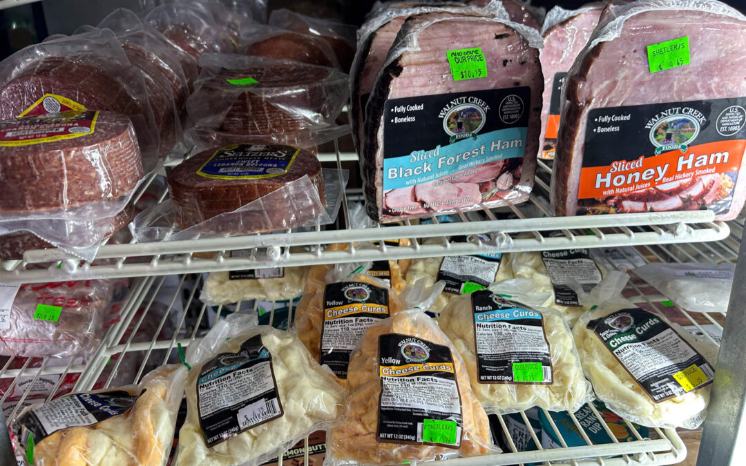 Shetler's Supplies Hardware Variety Bulk Foods Greenville PA Shelves in a refrigerator display assorted packaged deli meats and cheese, including sliced ham labeled Black Forest and Honey Ham, with green price stickers visible on most items.