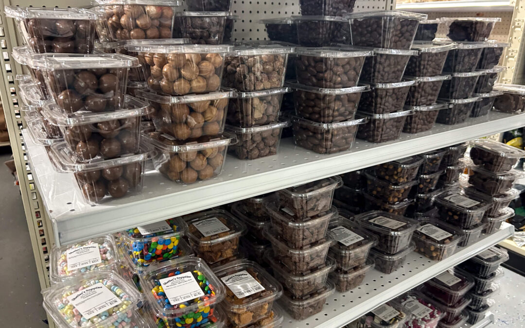 Shetler's Supplies Hardware Variety Bulk Foods Greenville PA Plastic containers filled with various chocolate-covered and candy-coated snacks are stacked on metal shelves in a store.